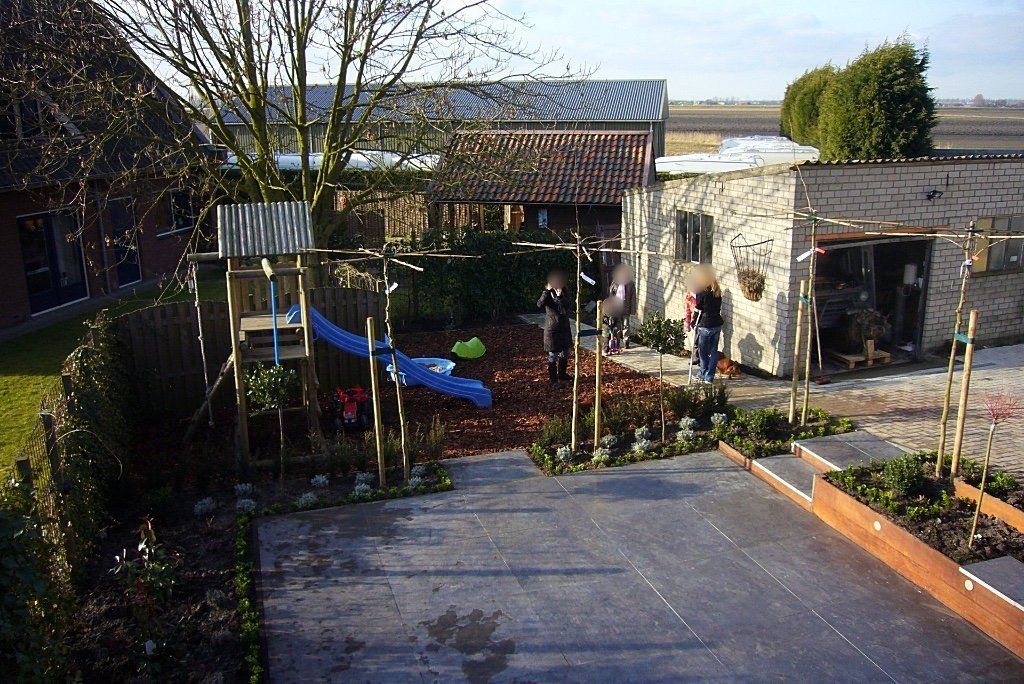 Achtertuin met speeltoestel, schuur en drie personen. Houten en stenen constructies, speelplek met houtsnippers.
