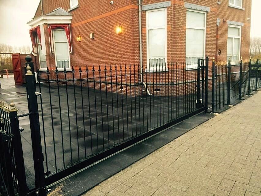 Een zwart smeedijzeren hek en poort voor een bakstenen gebouw.