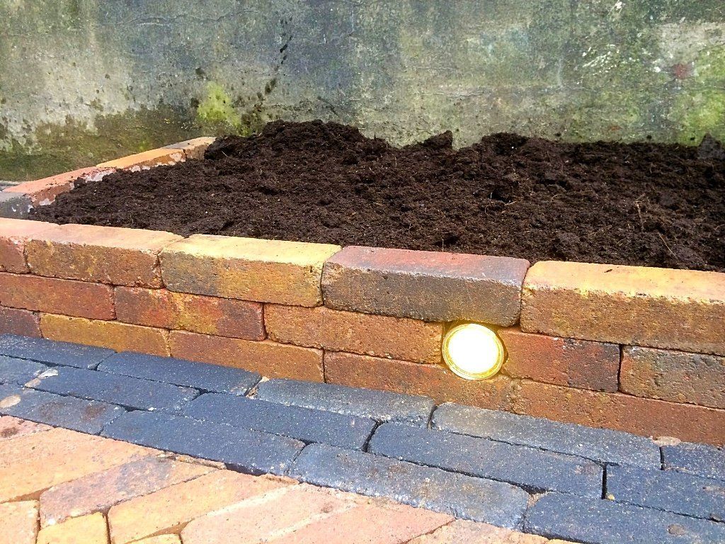 Verhoogd bakstenen tuinbed gevuld met donkere aarde, met een lamp.