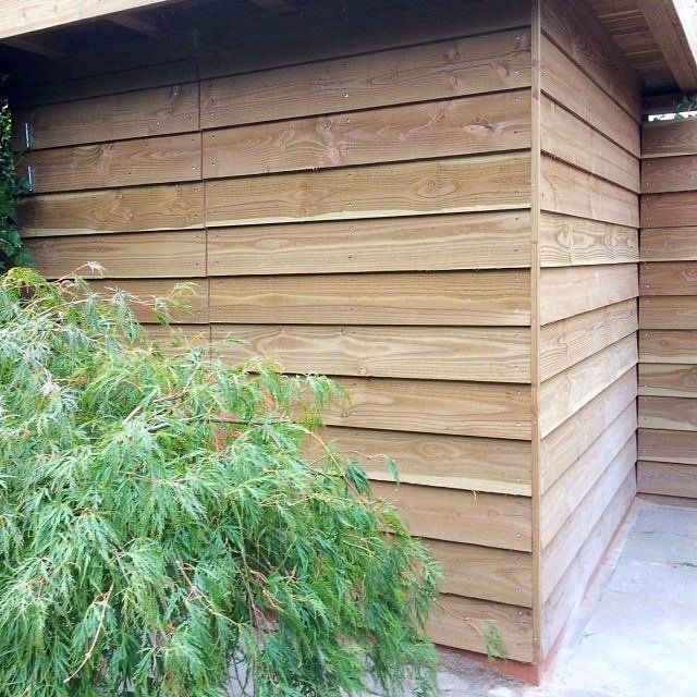 Buitenzijde van een houten schuur met horizontale gevelbekleding, hoekdetails en beplanting.