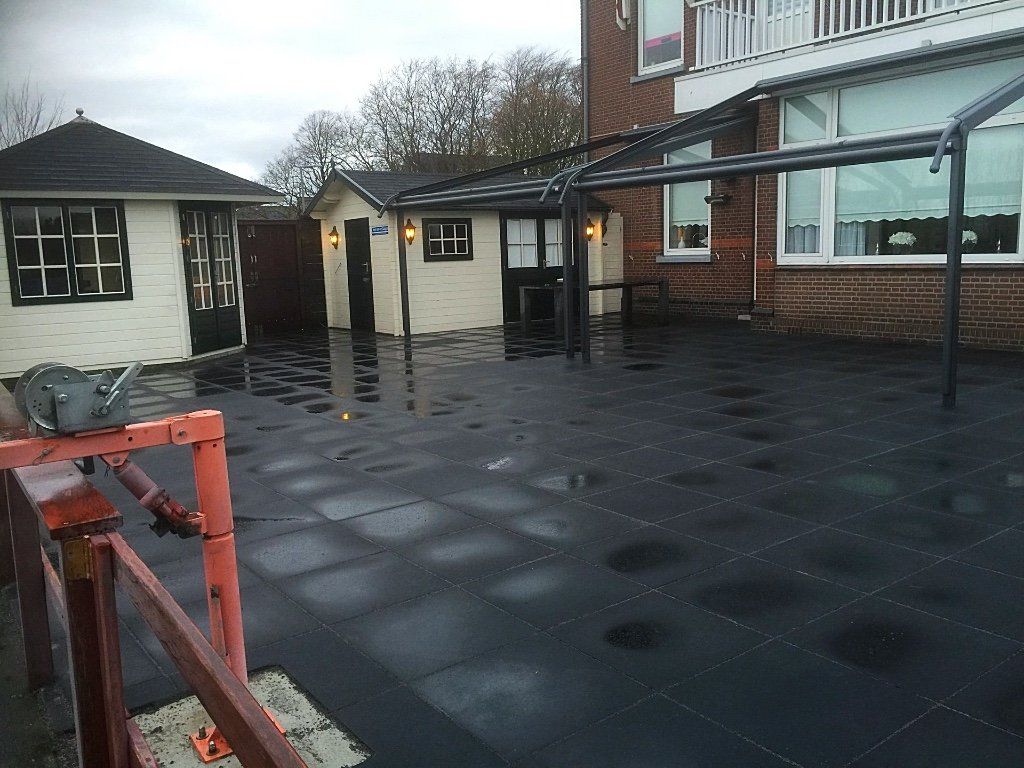 Buitenruimte met zwarte tegels, kleine gebouwen, een luifel en een oranje steiger. Natte ondergrond.
