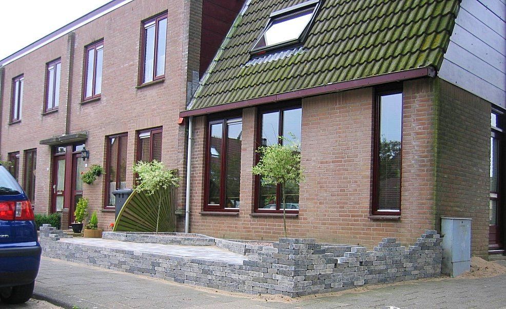 Bakstenen gebouw met een groen pannendak, ramen en een lage stenen muur.