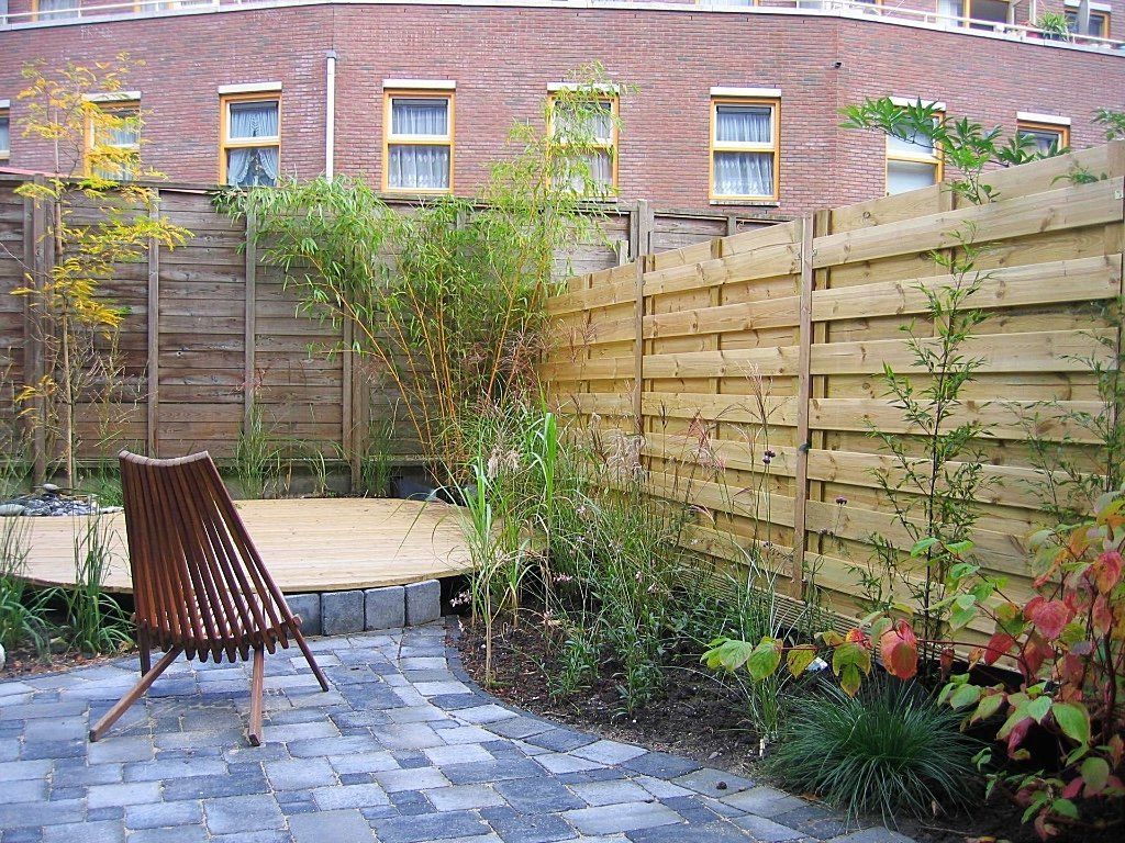 Achtertuin met houten schutting, stenen terras, vlonder, metalen stoel en planten.