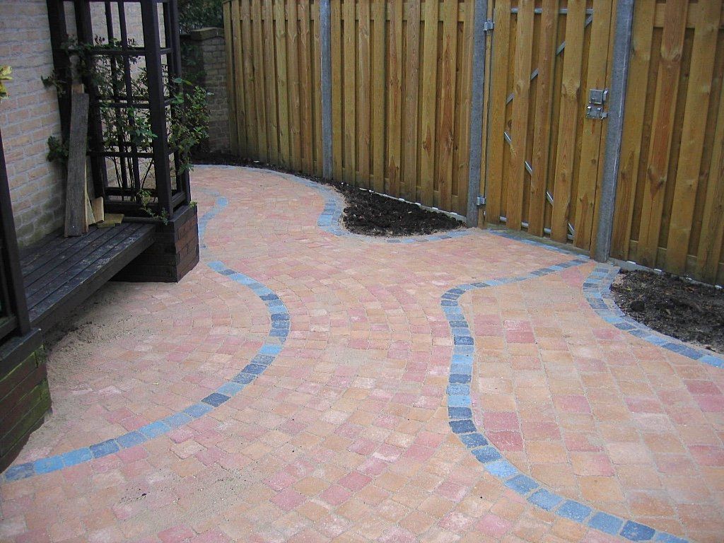 Bakstenen pad met gebogen blauwe randen, naast een houten hek en een zwart klimrek.