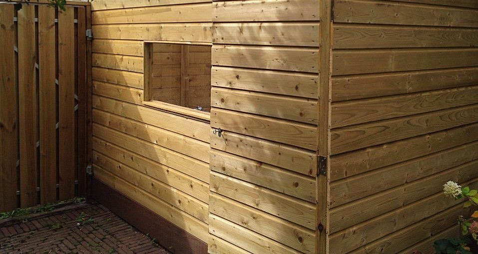 Houten schuur met een vierkant raam; bruine horizontale gevelbekleding.