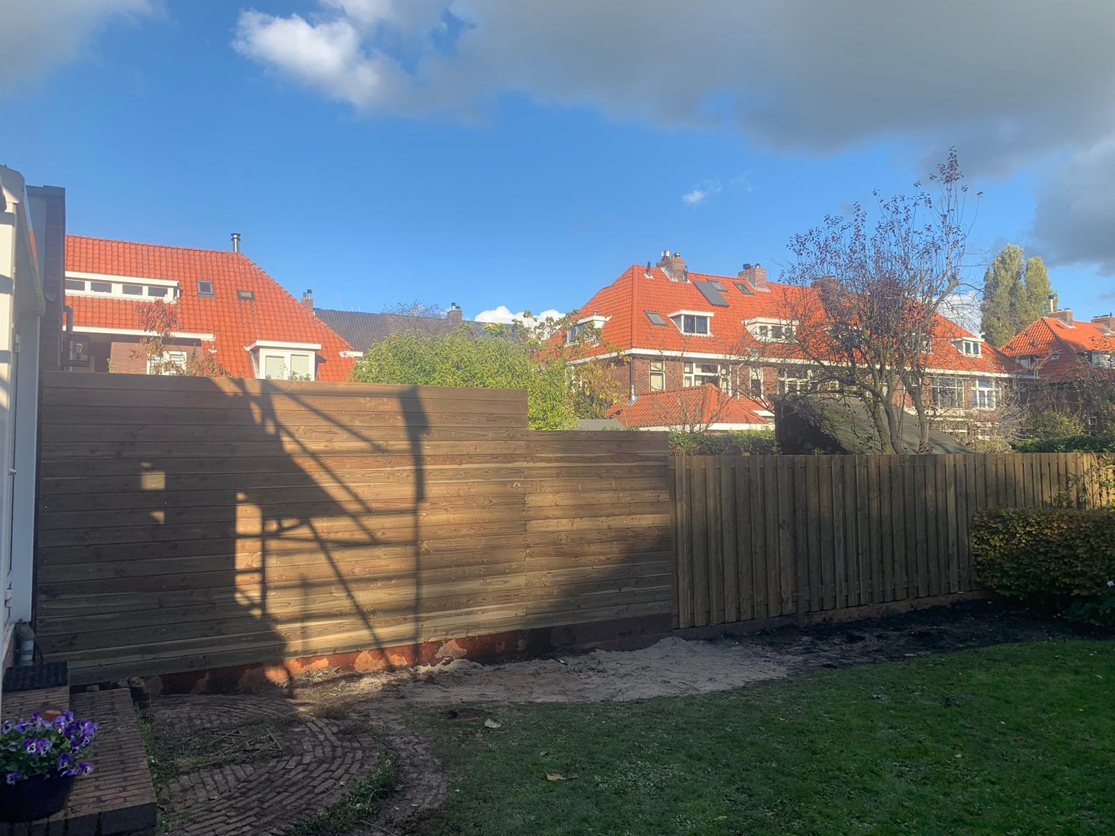 Houten schutting in een achtertuin met huizen en de lucht op de achtergrond. Zonnige dag.