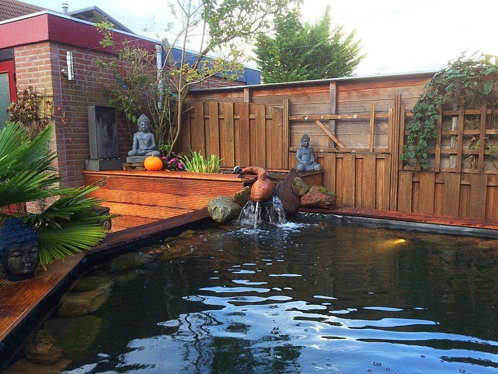 Vijver in de achtertuin met houten terras, waterval en Boeddhabeelden.