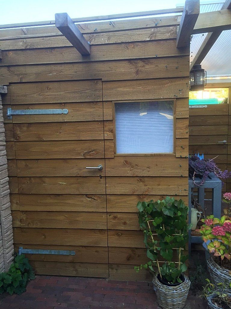 Houten schuurtje met klein raam, deur en planten. Bruine en beige tinten.
