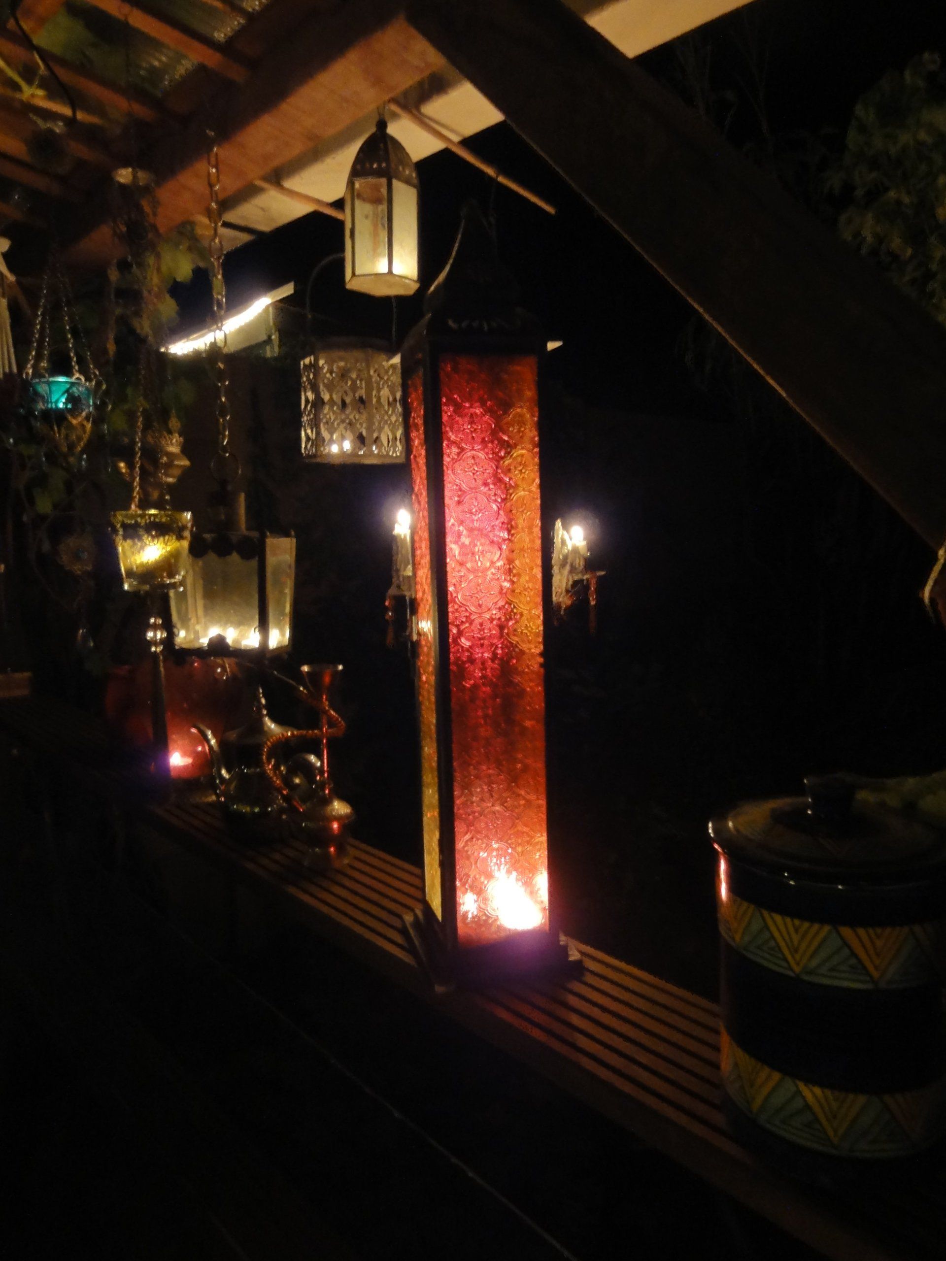 Een buitenscène 's nachts met verlichte lantaarns in verschillende vormen en kleuren langs een houten richel, die een warme, uitnodigende sfeer creëren.