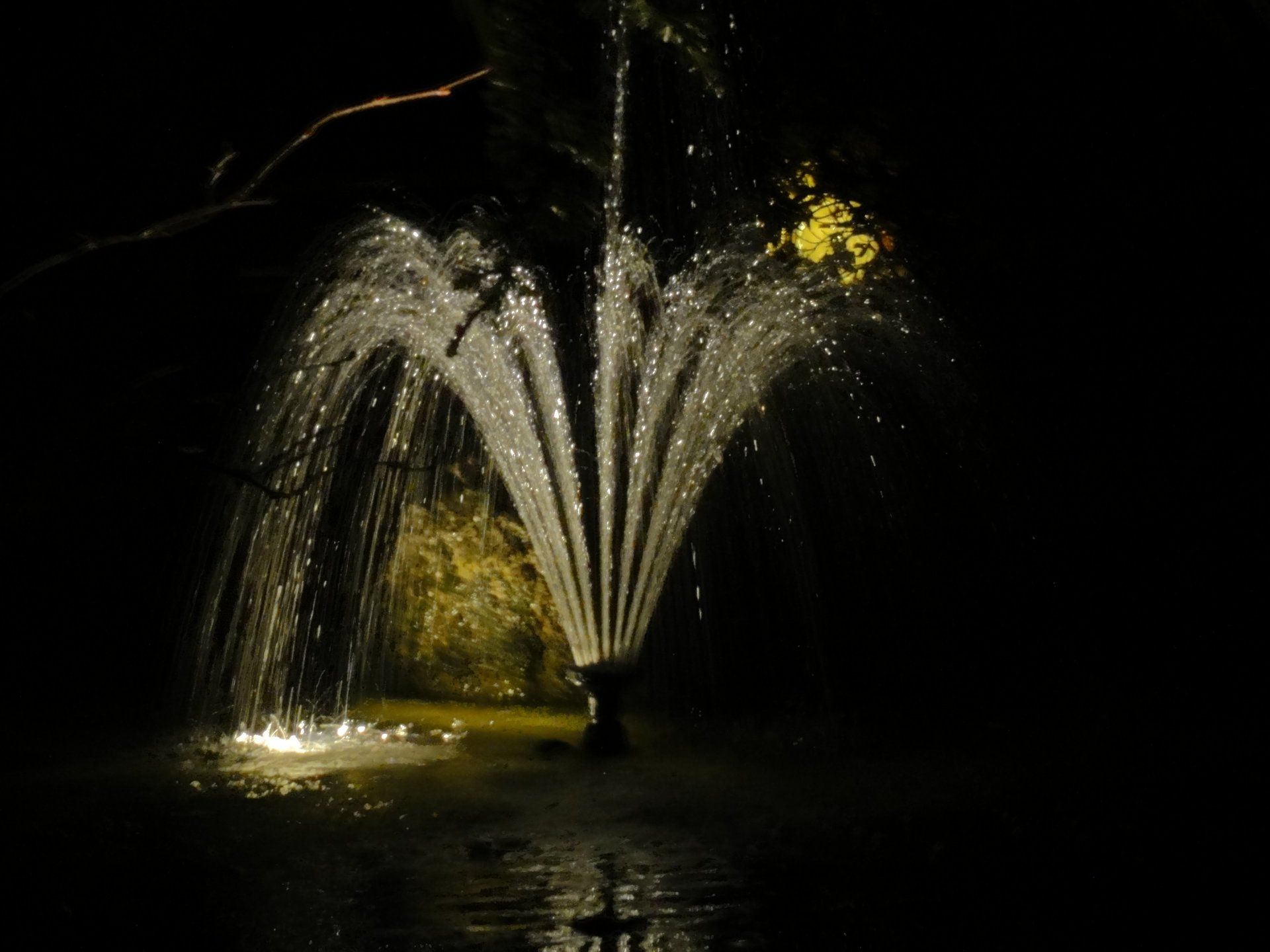 Fontein met spuitend water, verlicht 's nachts, donkere achtergrond.