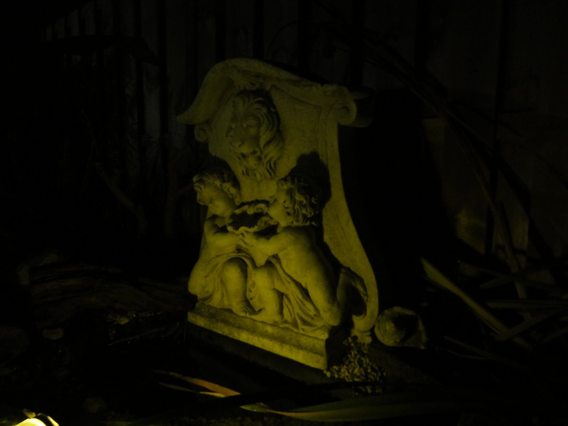 Stenen sculptuur van twee cherubijnen onder een gedrapeerde banner, verlicht in een donkere omgeving.