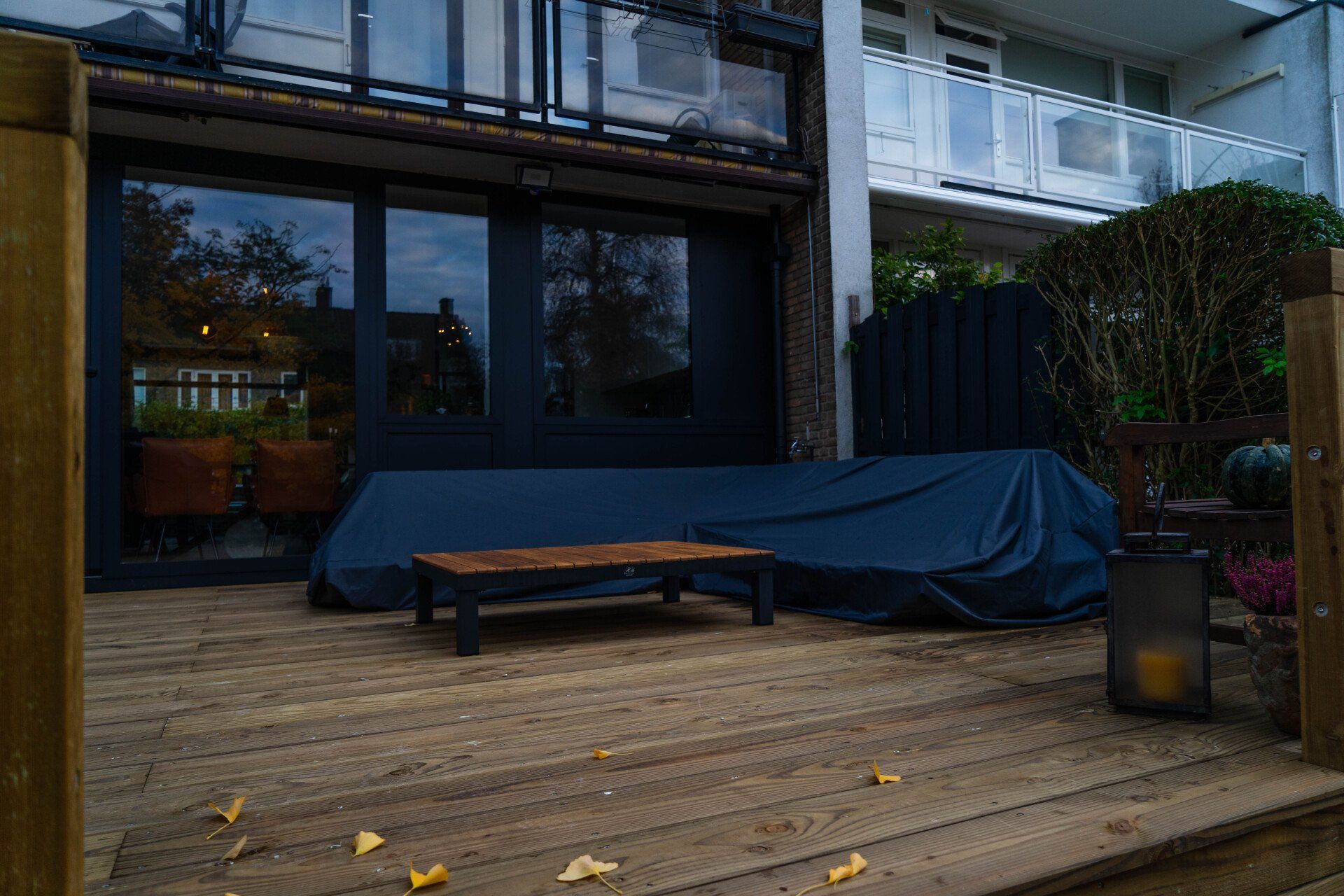 Houten terras met overdekte zithoek en bank; woongebouw op de achtergrond.