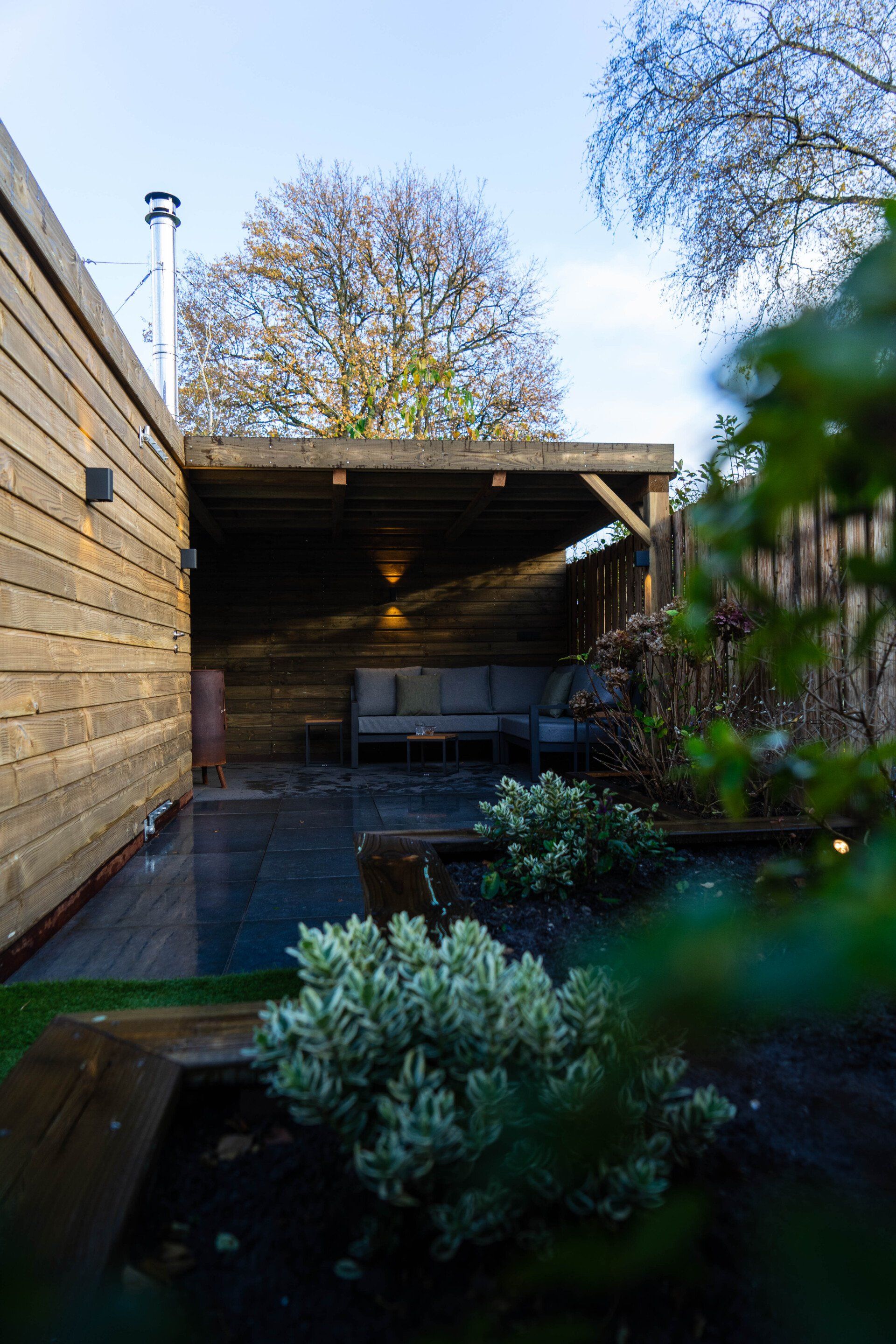 Buiten zitgedeelte met een houten pergola, een bank en planten.