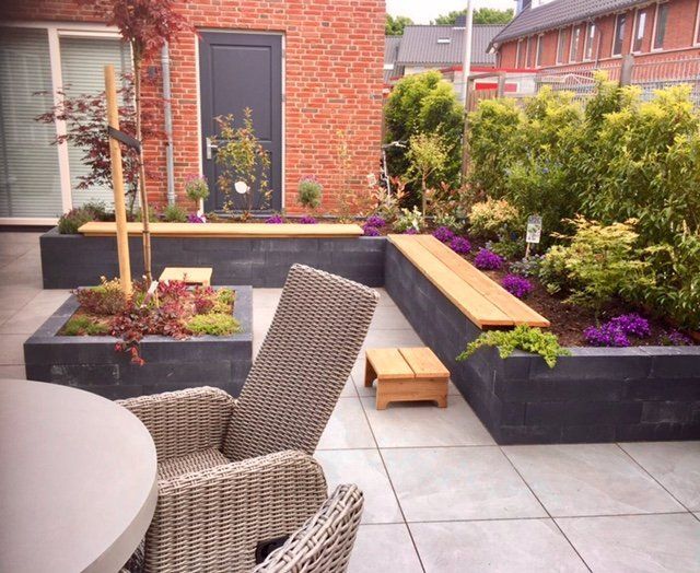 Terras met ingebouwde plantenbakken, banken en zitgelegenheid buiten. Bakstenen gebouw, natuurstenen bestrating en weelderig groen.