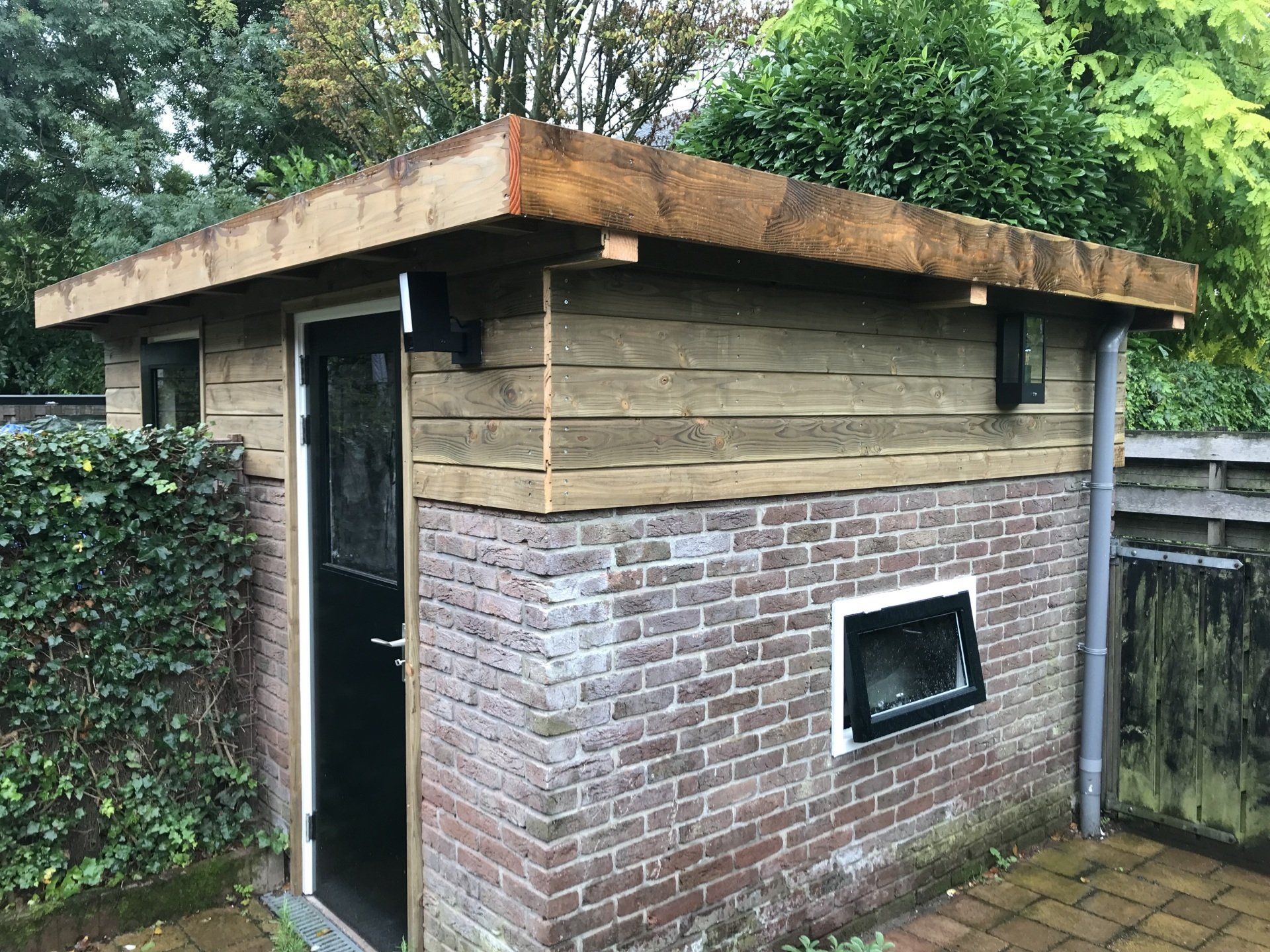 Klein houten schuurtje met bakstenen fundering, deur en ramen.