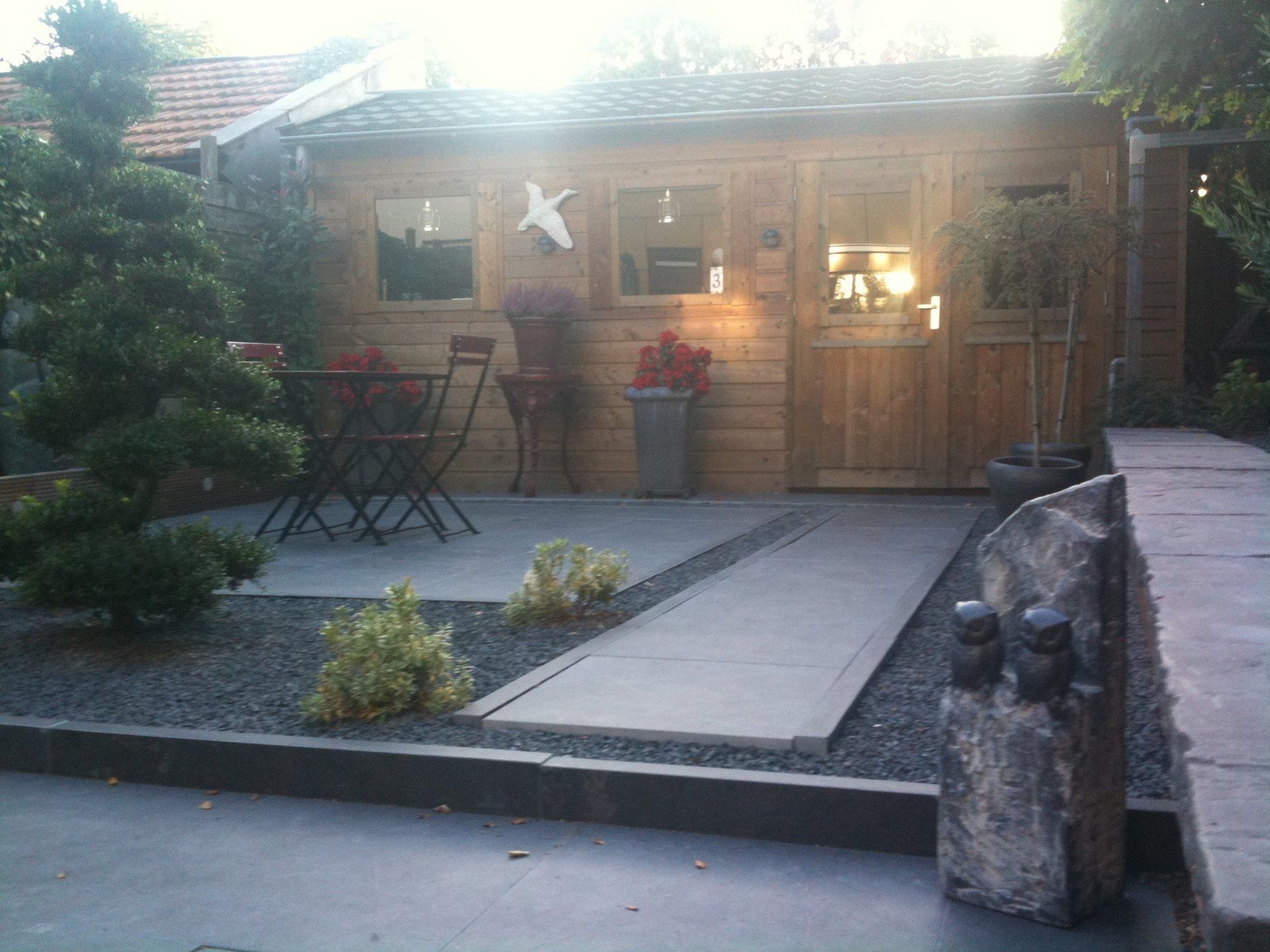 Houten schuur met terrasmeubilair, grindpad en aangelegde tuin.