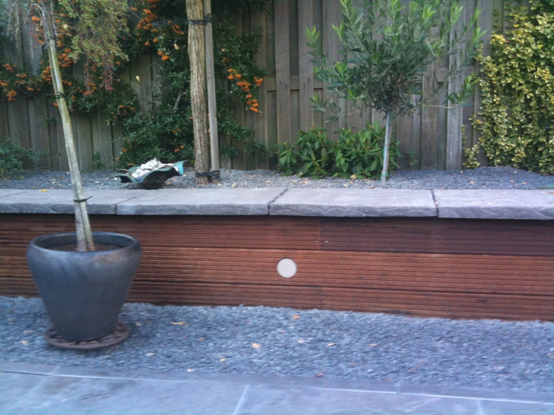 Verhoogd tuinbed met houten lambrisering, grind en potplanten.