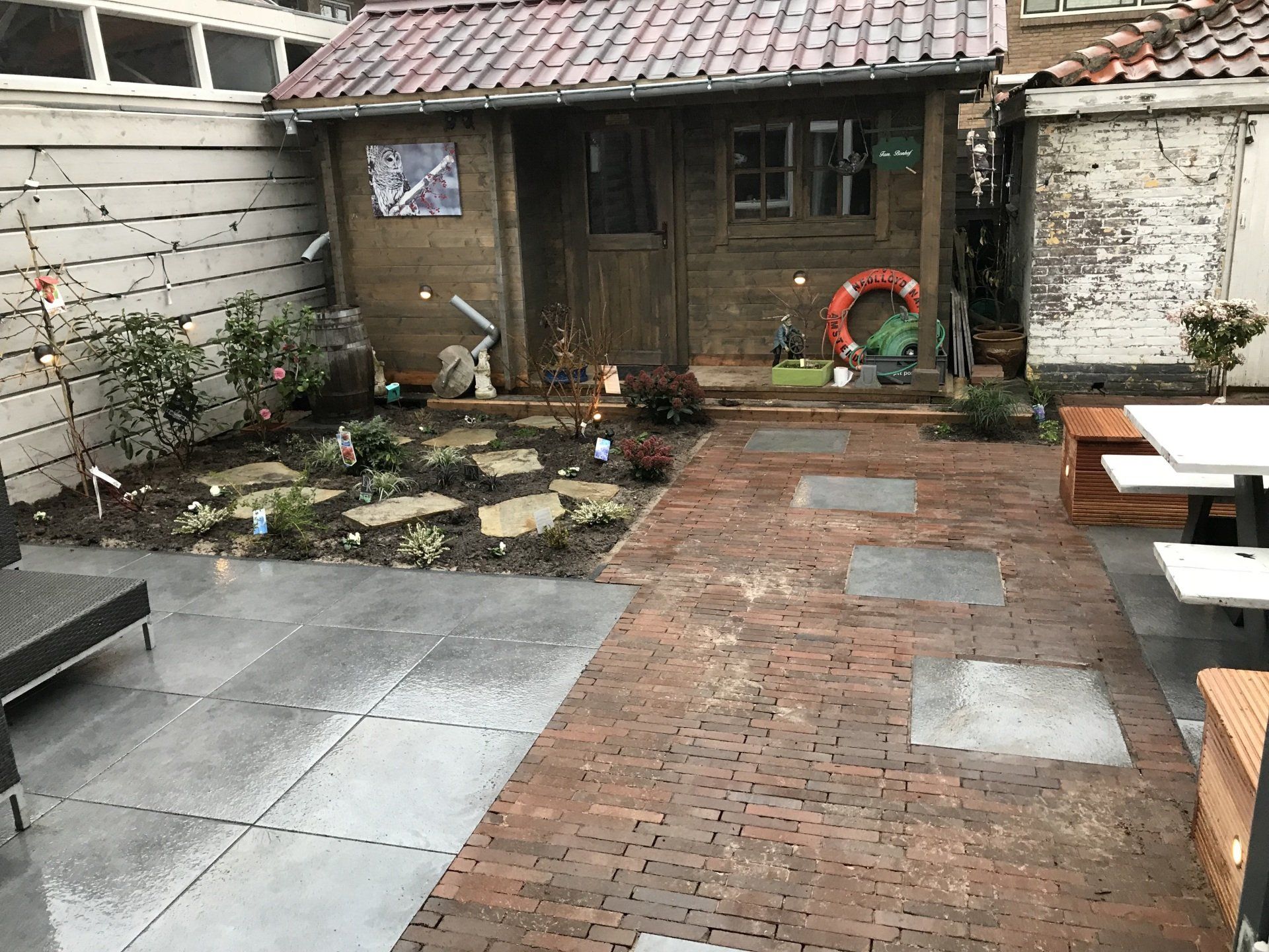 Terras in de achtertuin met een bakstenen pad dat leidt naar een houten schuur en de tuin.