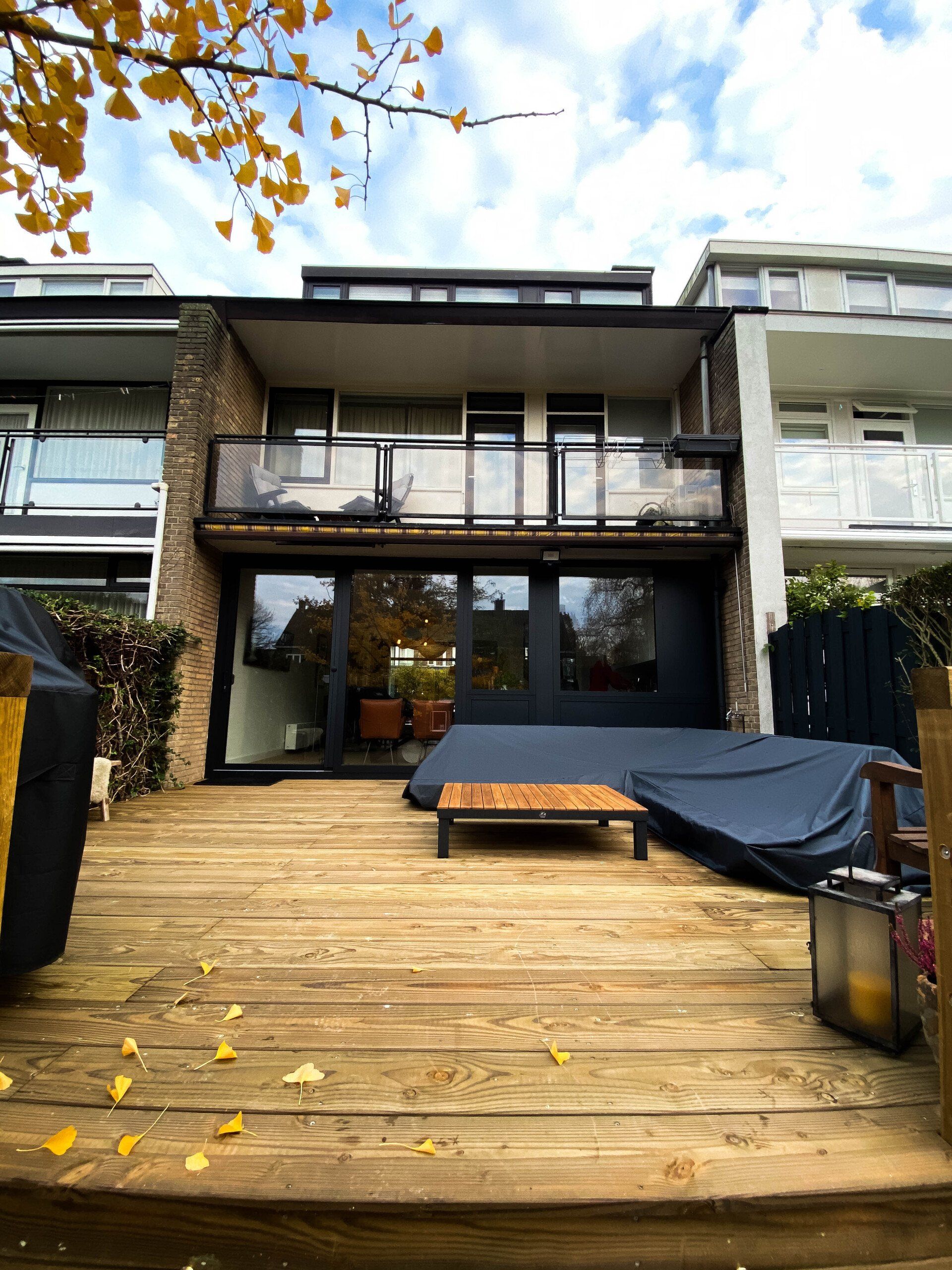 Houten terras met een huis van meerdere verdiepingen, balkon en overdekt tuinmeubilair.