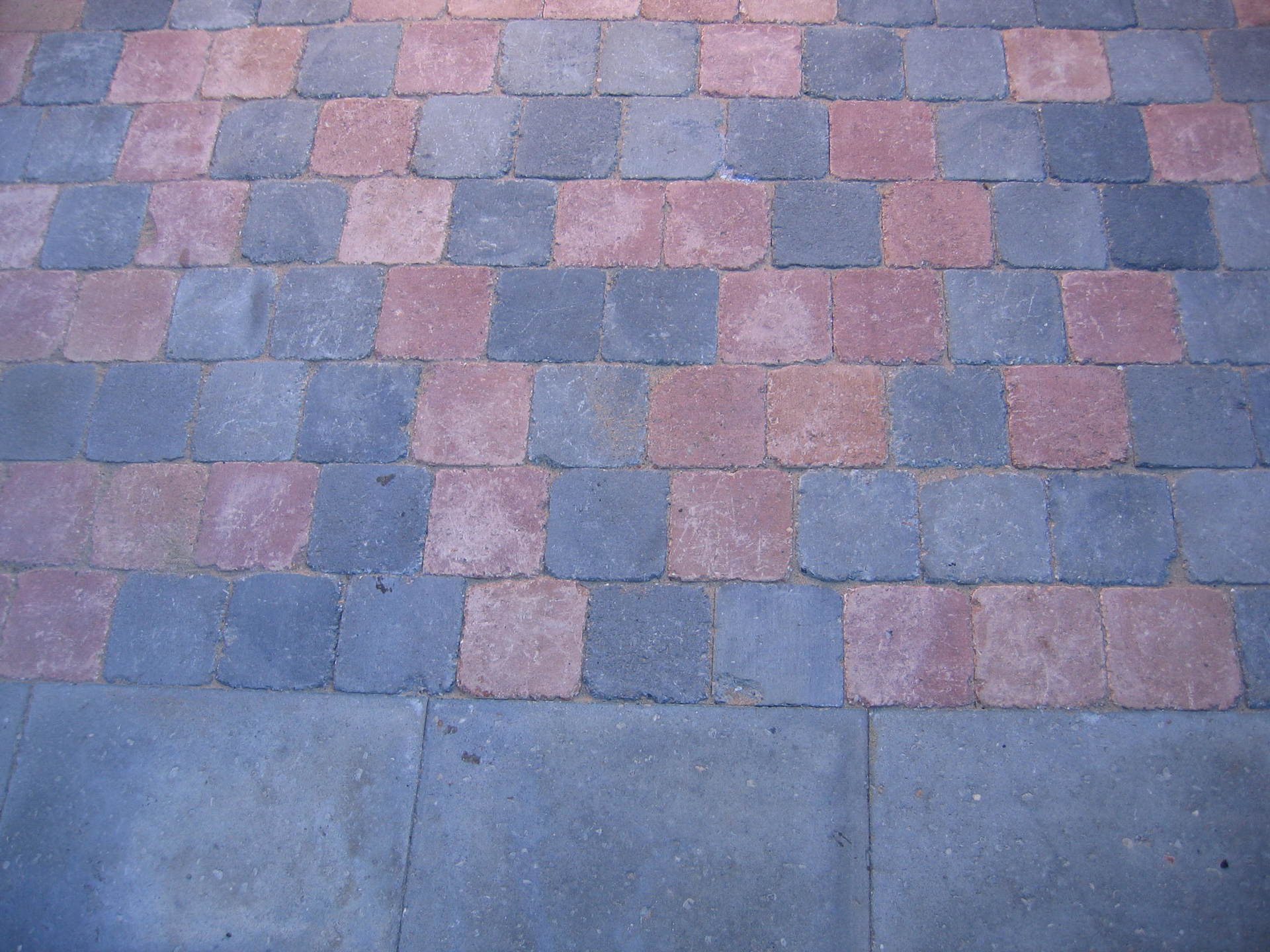 Een terras van bakstenen met afwisselend rode en blauwgrijze bakstenen, dat overgaat in een effen grijze betonnen rand.