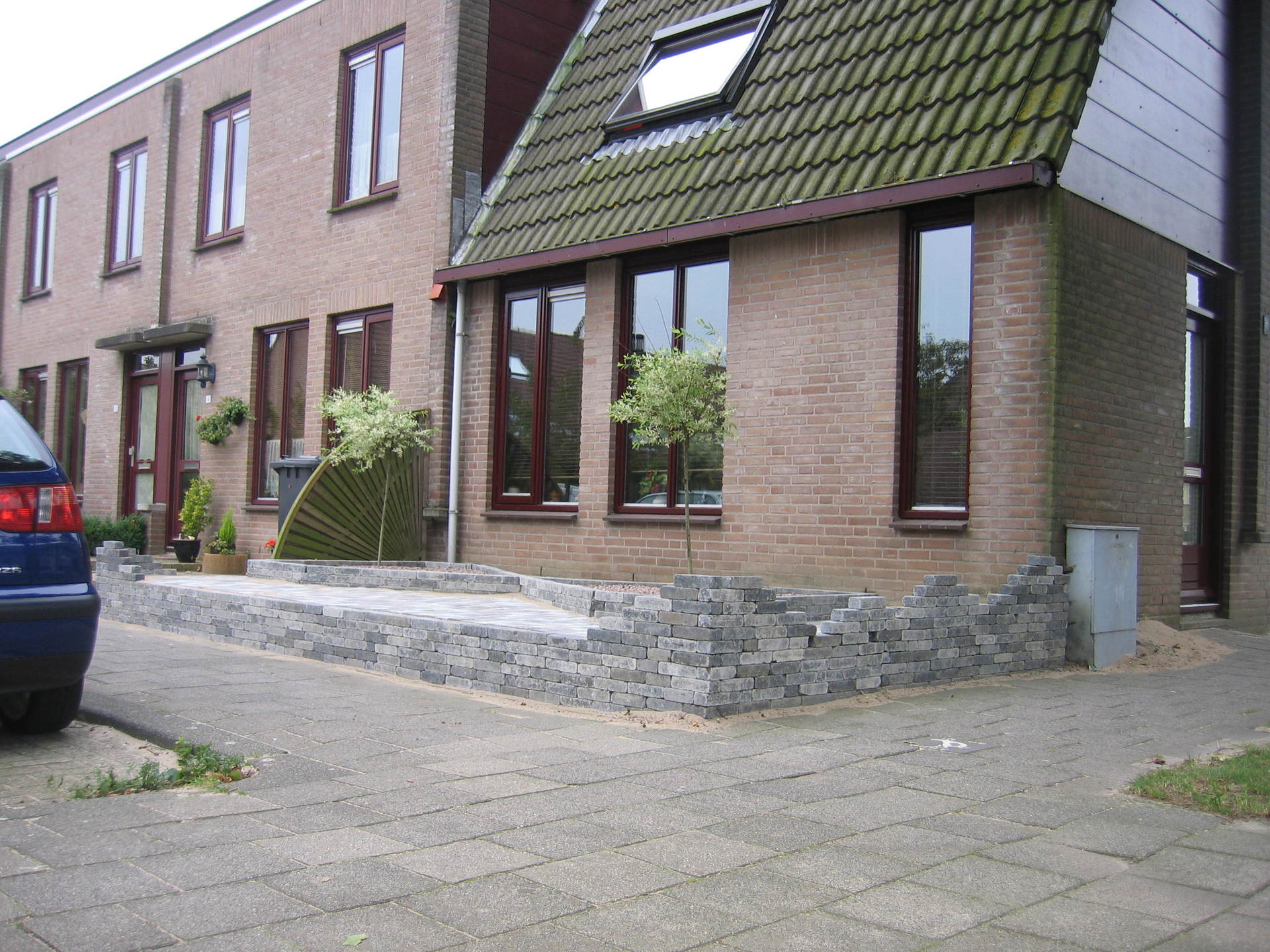 De buitenkant van een bakstenen gebouw met een stenen keermuur en een auto ervoor geparkeerd.
