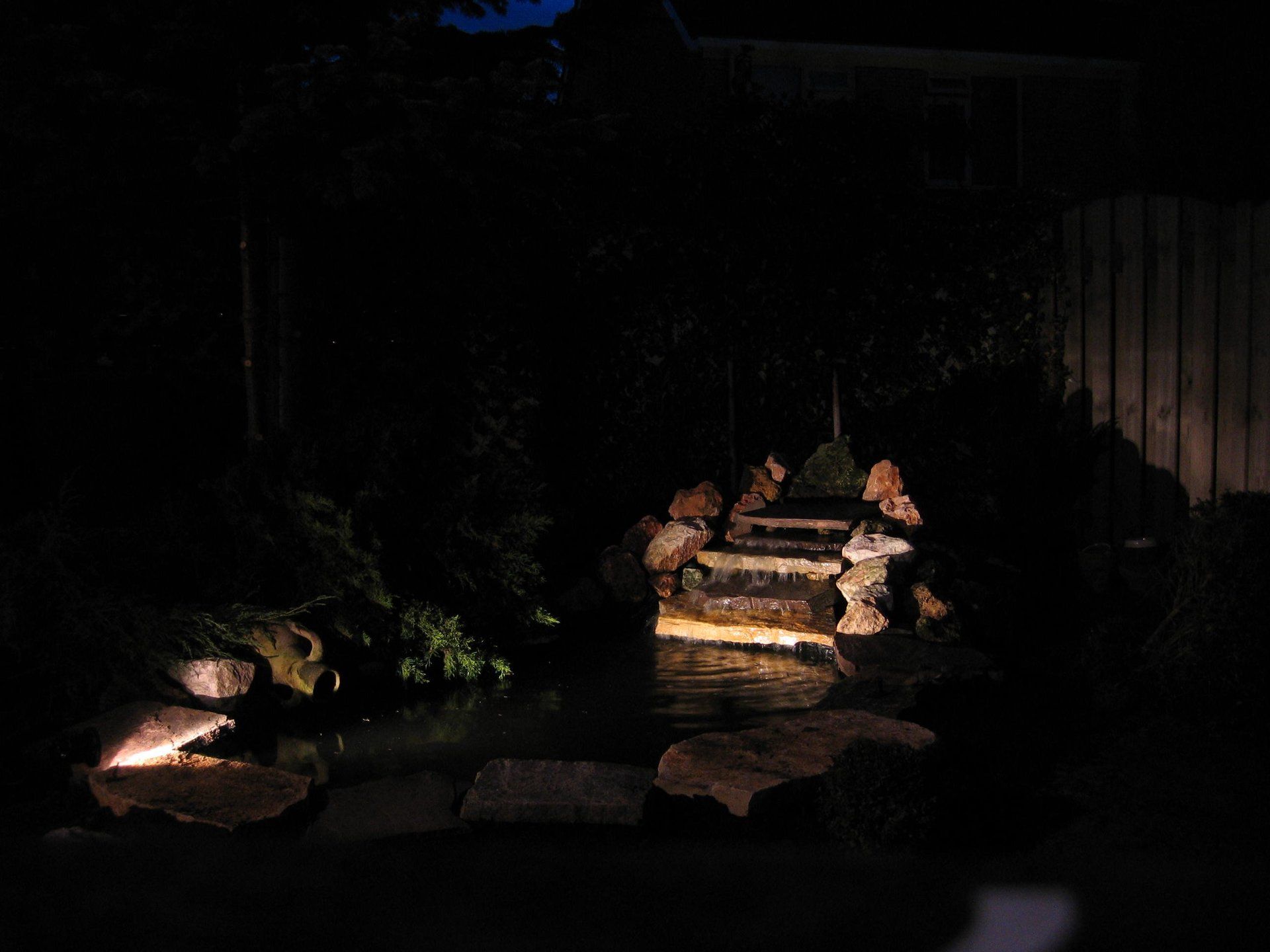 Een nachtelijk uitzicht op een kleine, verlichte waterval in een tuin.