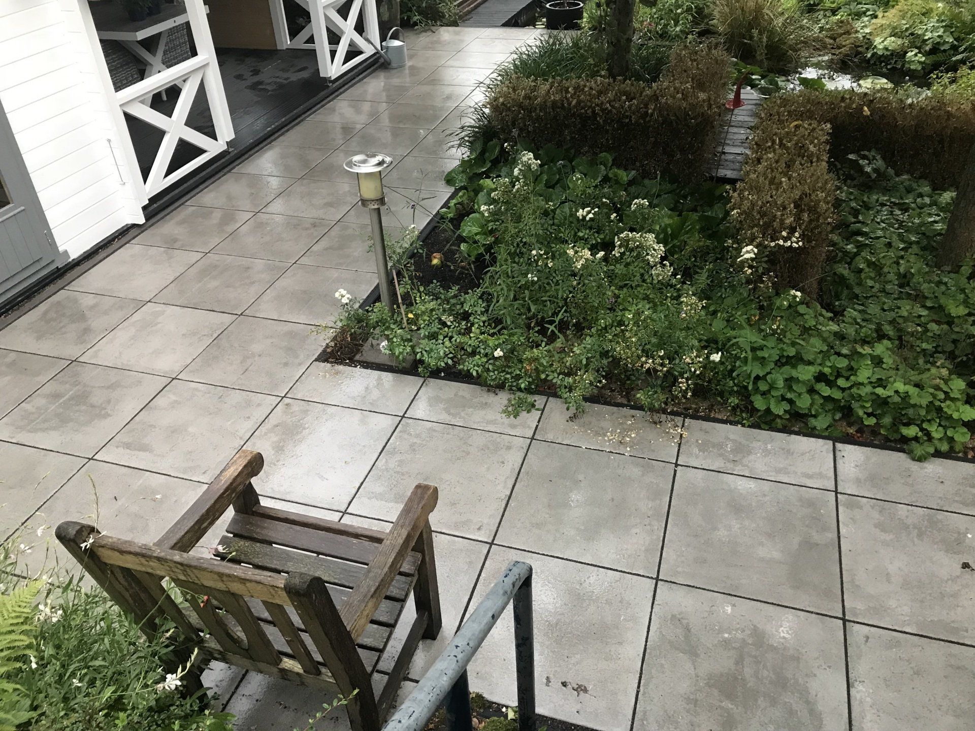 Een geplaveid pad met een houten stoel en kleine bloembedden.