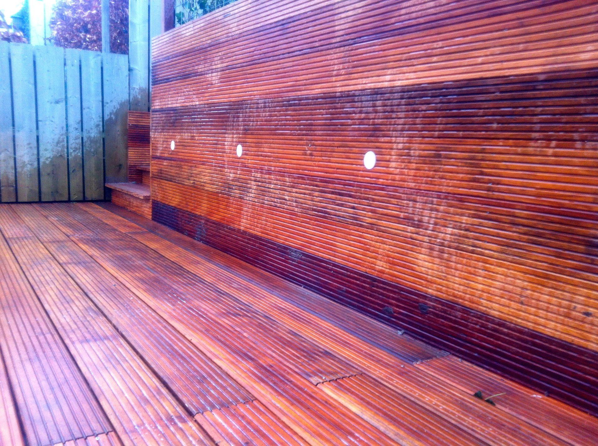 Houten terras en muur met drie kleine lampjes; buiten, schemering.