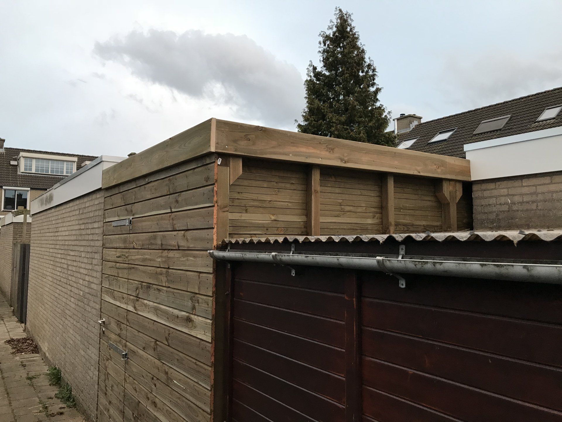 Houten hek met een plat dak boven een poort, onder een bewolkte hemel.