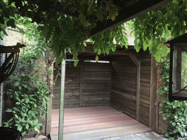 Houten constructie met een roodachtige vloer, omgeven door weelderig groen.