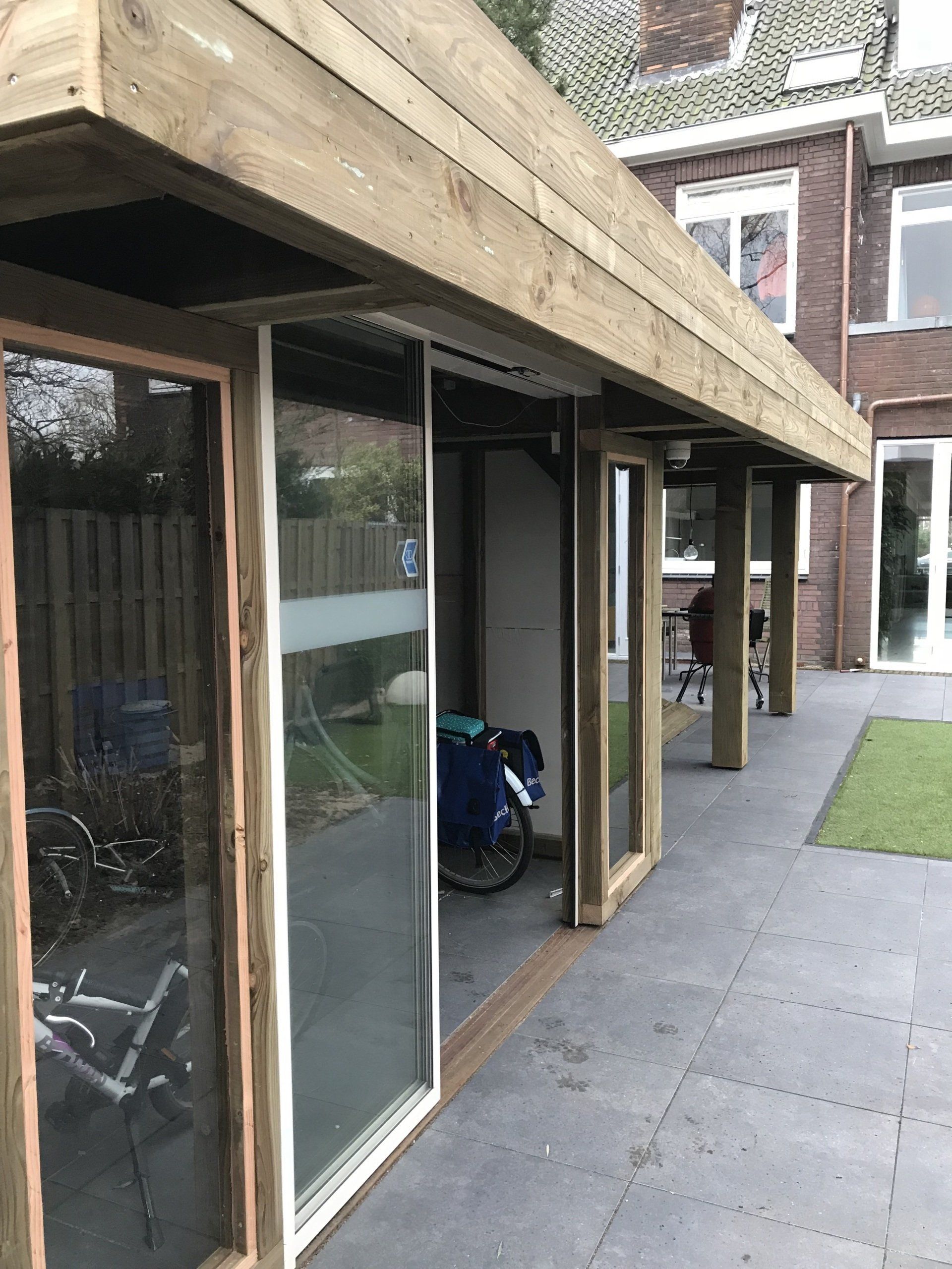 Houten terras met schuifdeuren van glas, overkapping, fietsenstalling en uitzicht op de achtertuin.