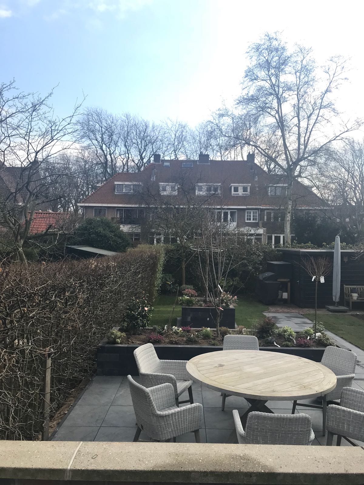 Terras met ronde tafel en stoelen, met uitzicht op een tuin met groen en huizen in de verte.