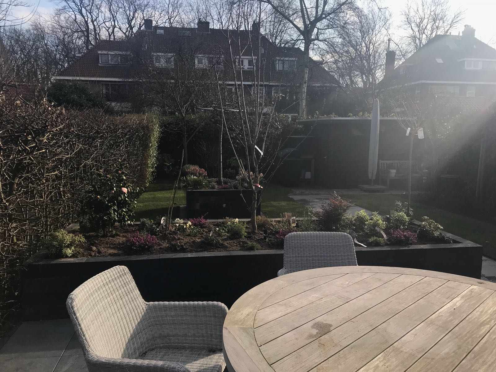 Terras met tafel en stoel, bloembed en een huis op de achtergrond. Zonnige dag.