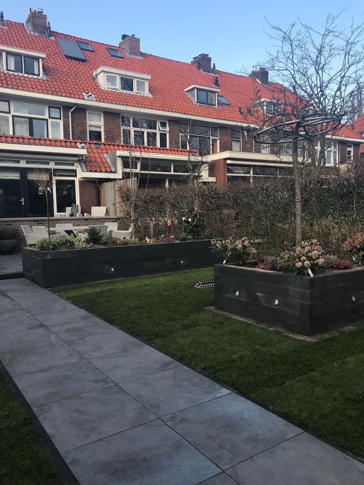 Rijtjeshuizen met rode pannendaken, bloemperken en een grijs stenen pad.