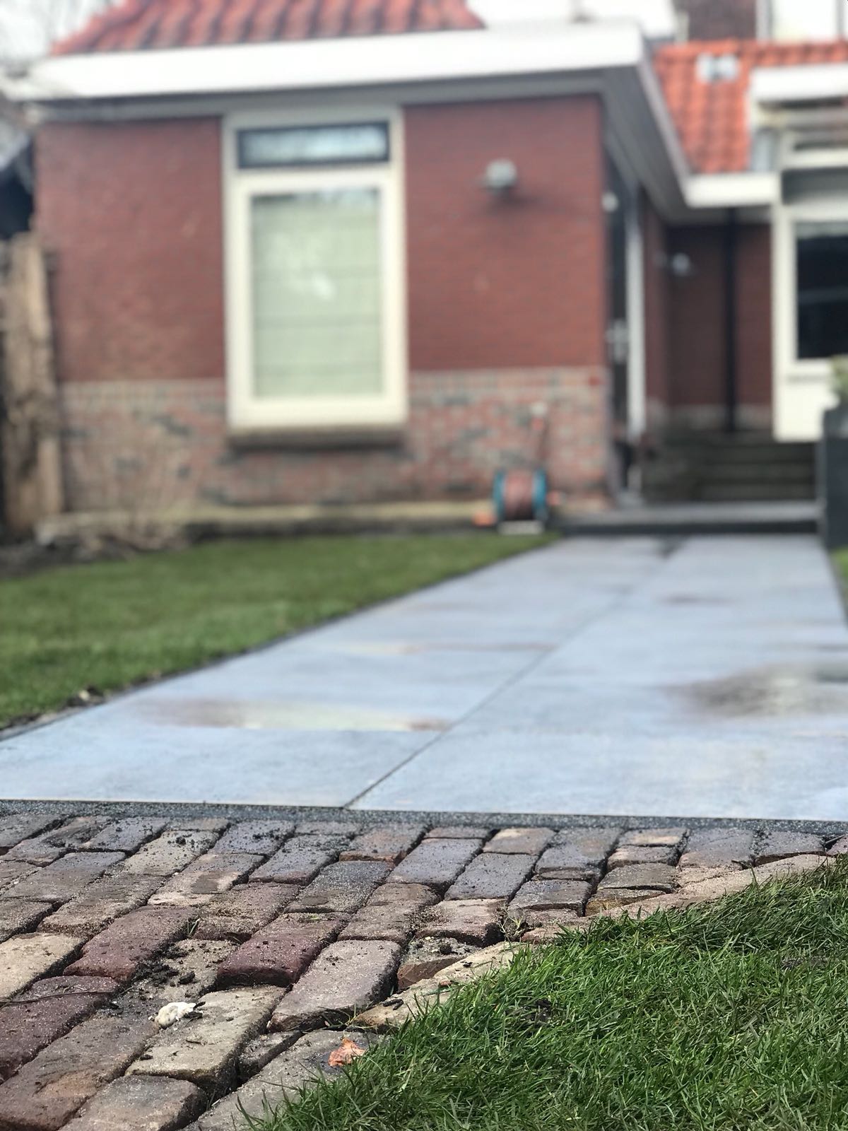 Een bakstenen pad leidt naar een huis met een bakstenen gevel, grenzend aan een groen gazon.