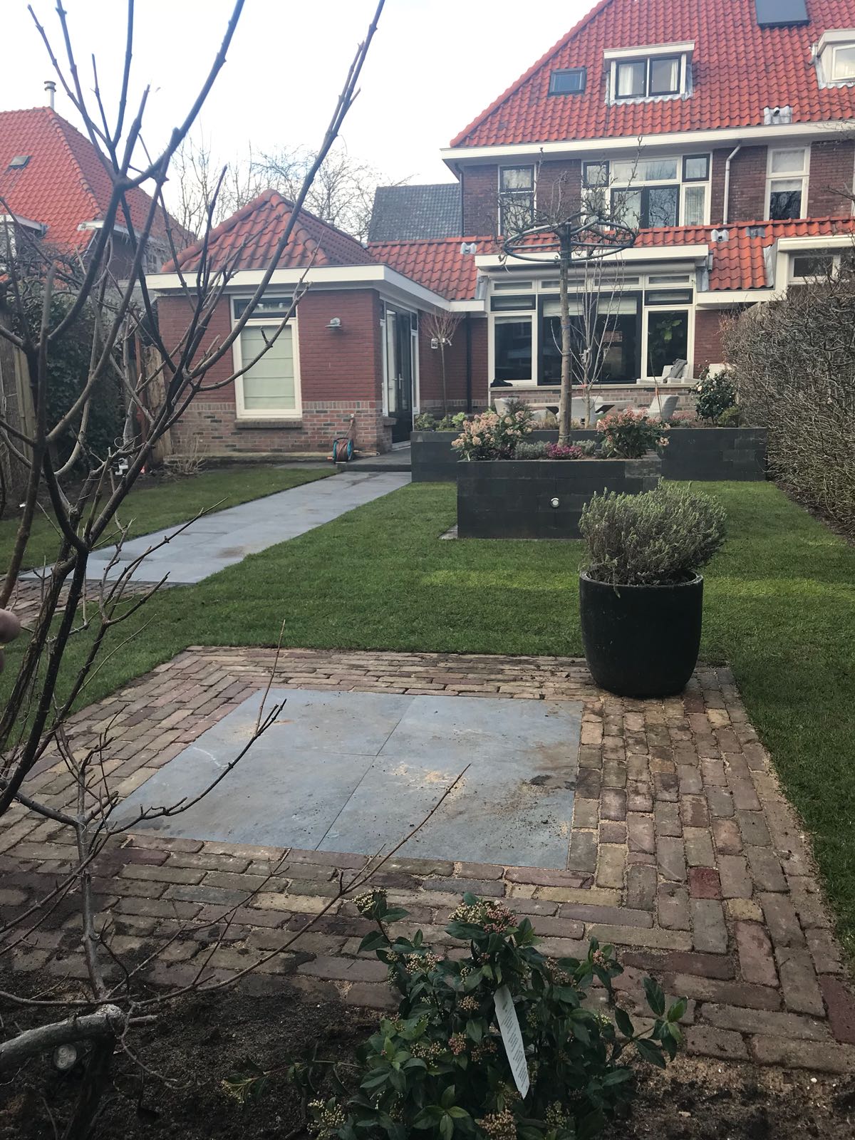 Achtertuin met stenen terras, gazon en huis met rood dak.