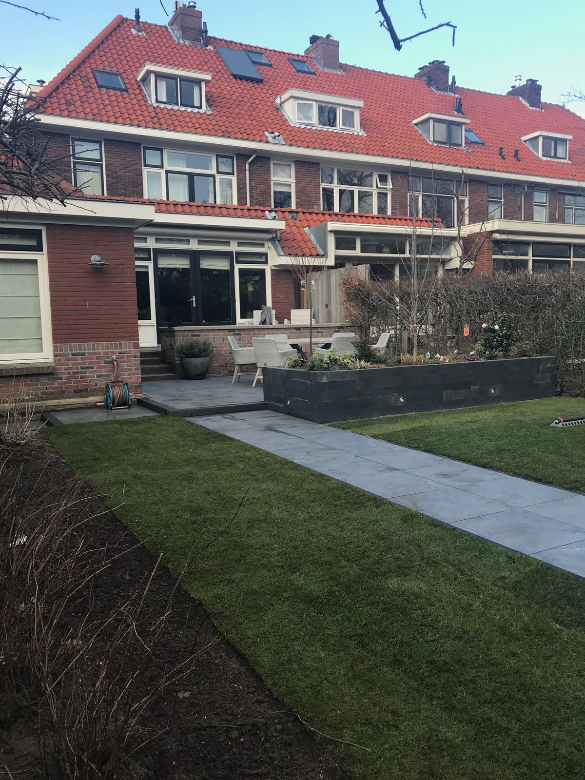 Rij bakstenen huizen met rode pannendaken. Voortuinen met donkergrijze paden en groen gras.