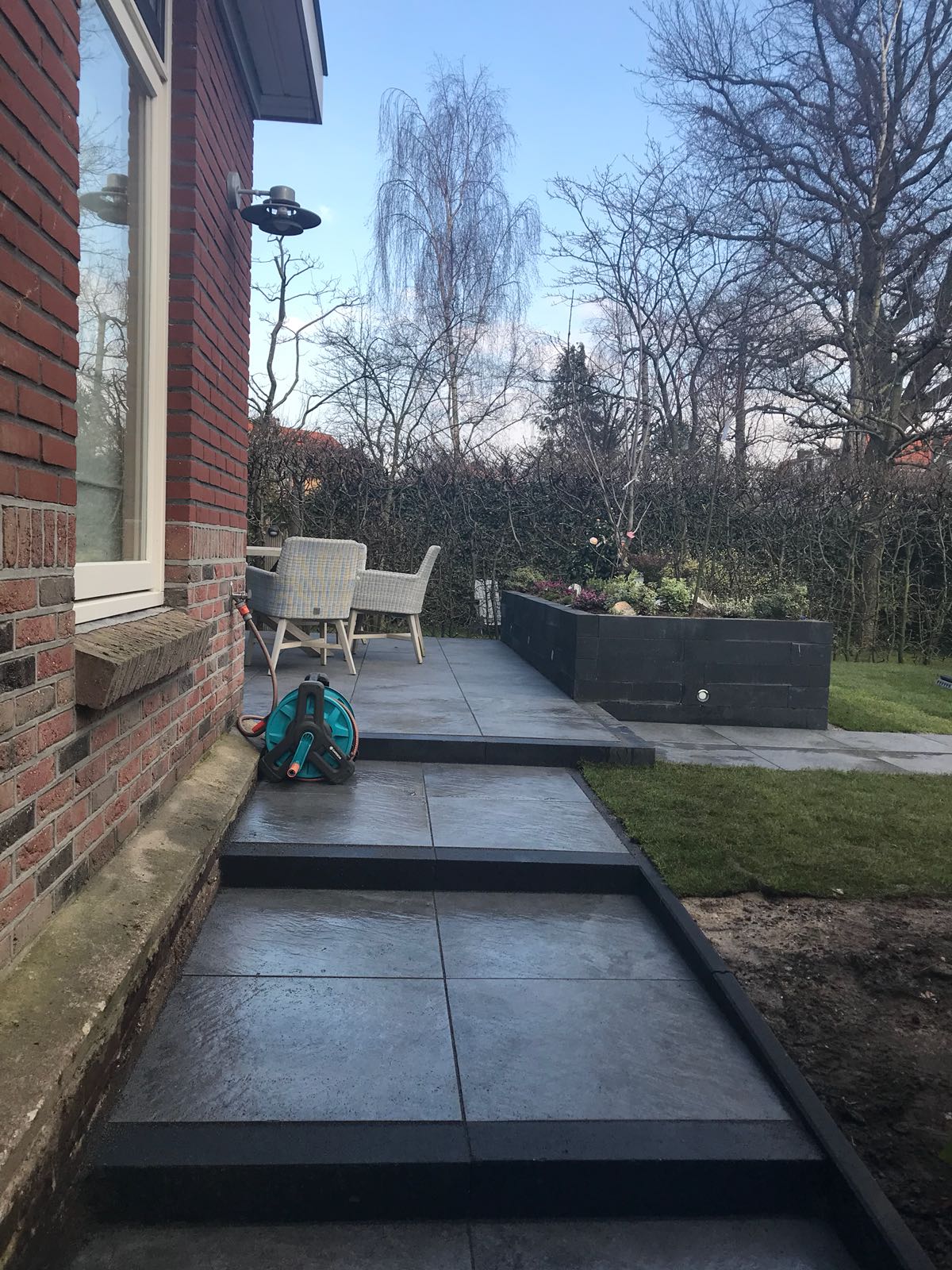 Buitenaanzicht: Bakstenen gebouw met terras en trap naar een verhoogd tuinbed en gazon.