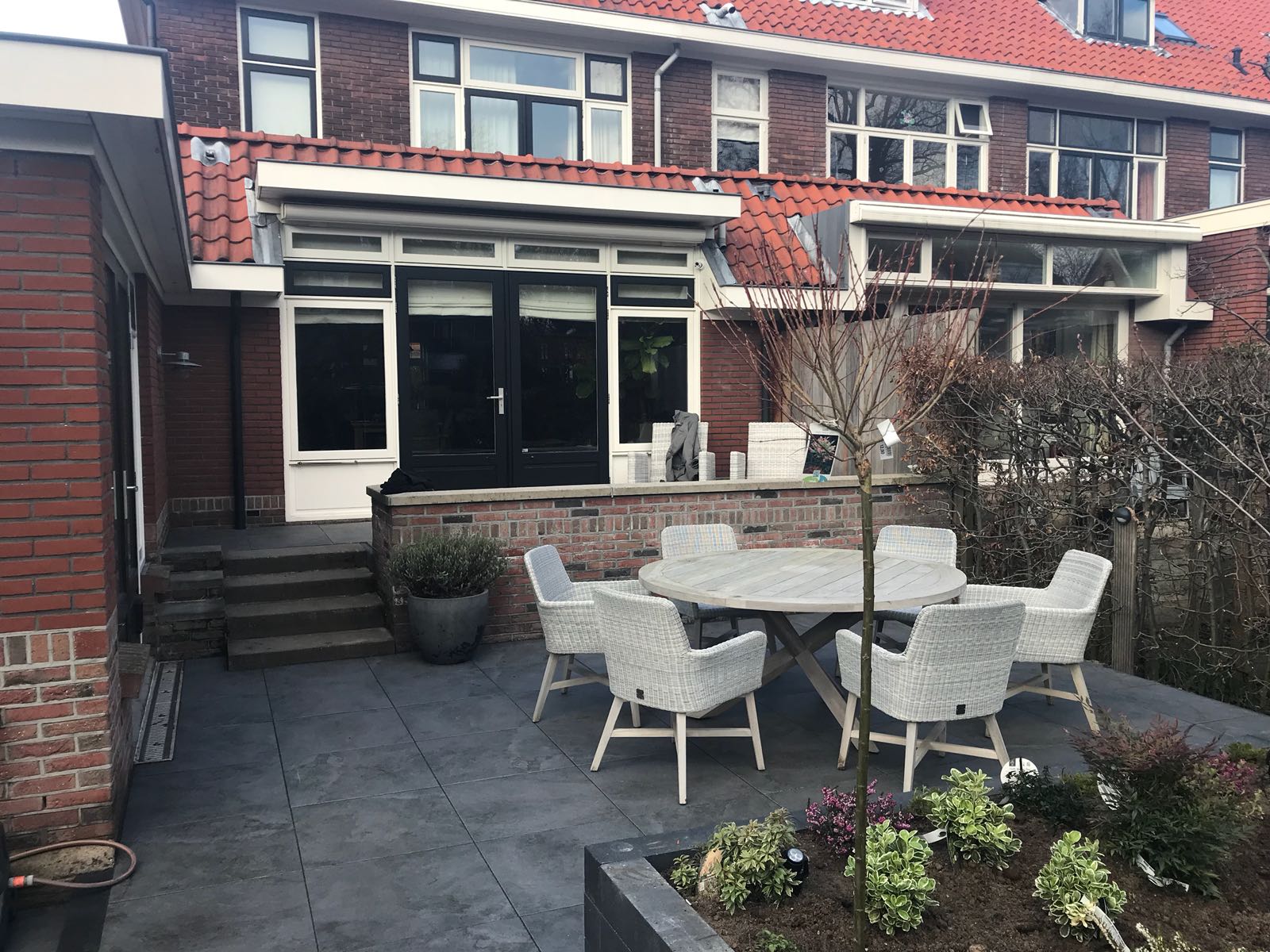 Terras in de achtertuin met een tafel, stoelen en een bakstenen huisje.