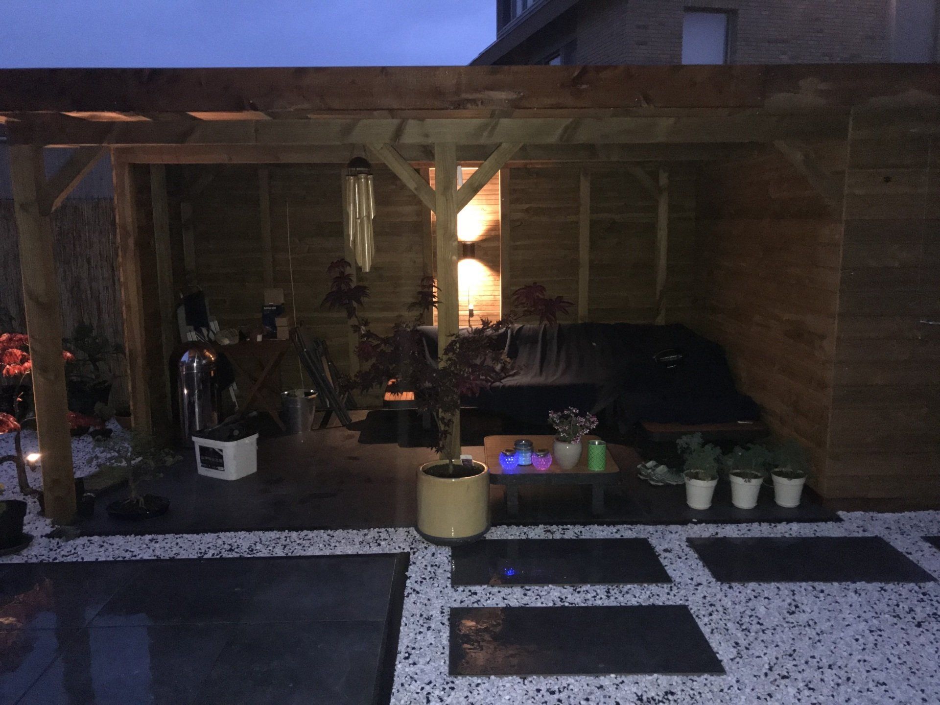Houten pergola voor buiten met zitgedeelte, planten en schijnwerpers; nachtscène.