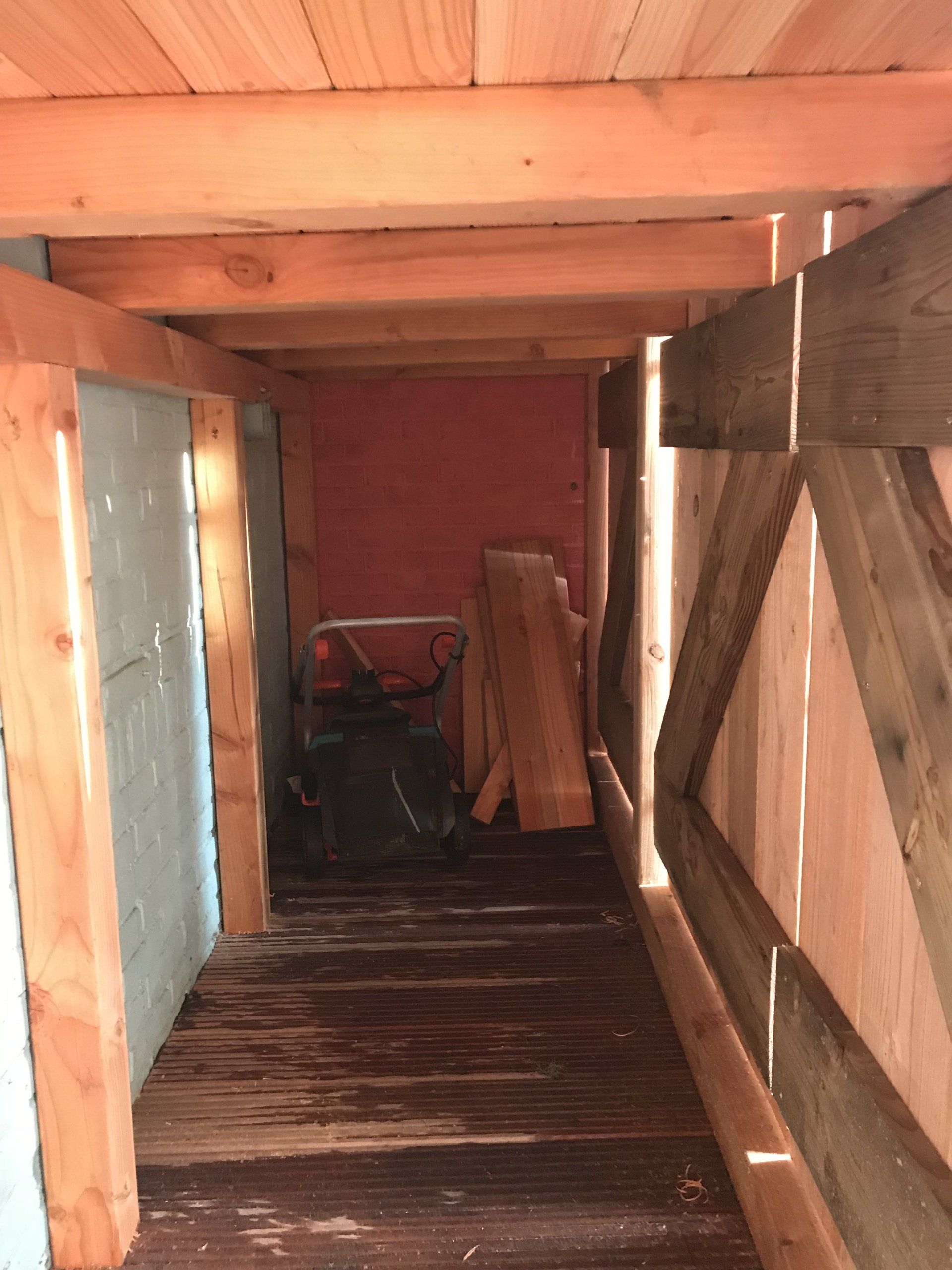 Interieurfoto van een houten schuur met een smalle doorgang, een rode achterwand en opgestapeld hout.