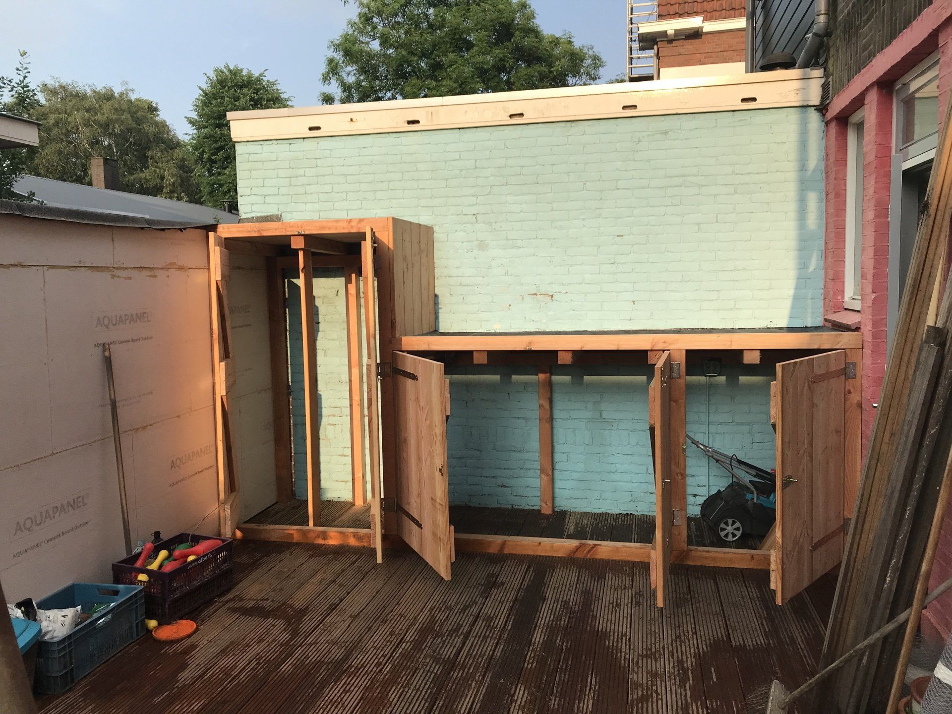 De bouw van houten opslagconstructies met blauwe isolatie op een terras. Gereedschap en bouwmaterialen zijn aanwezig.