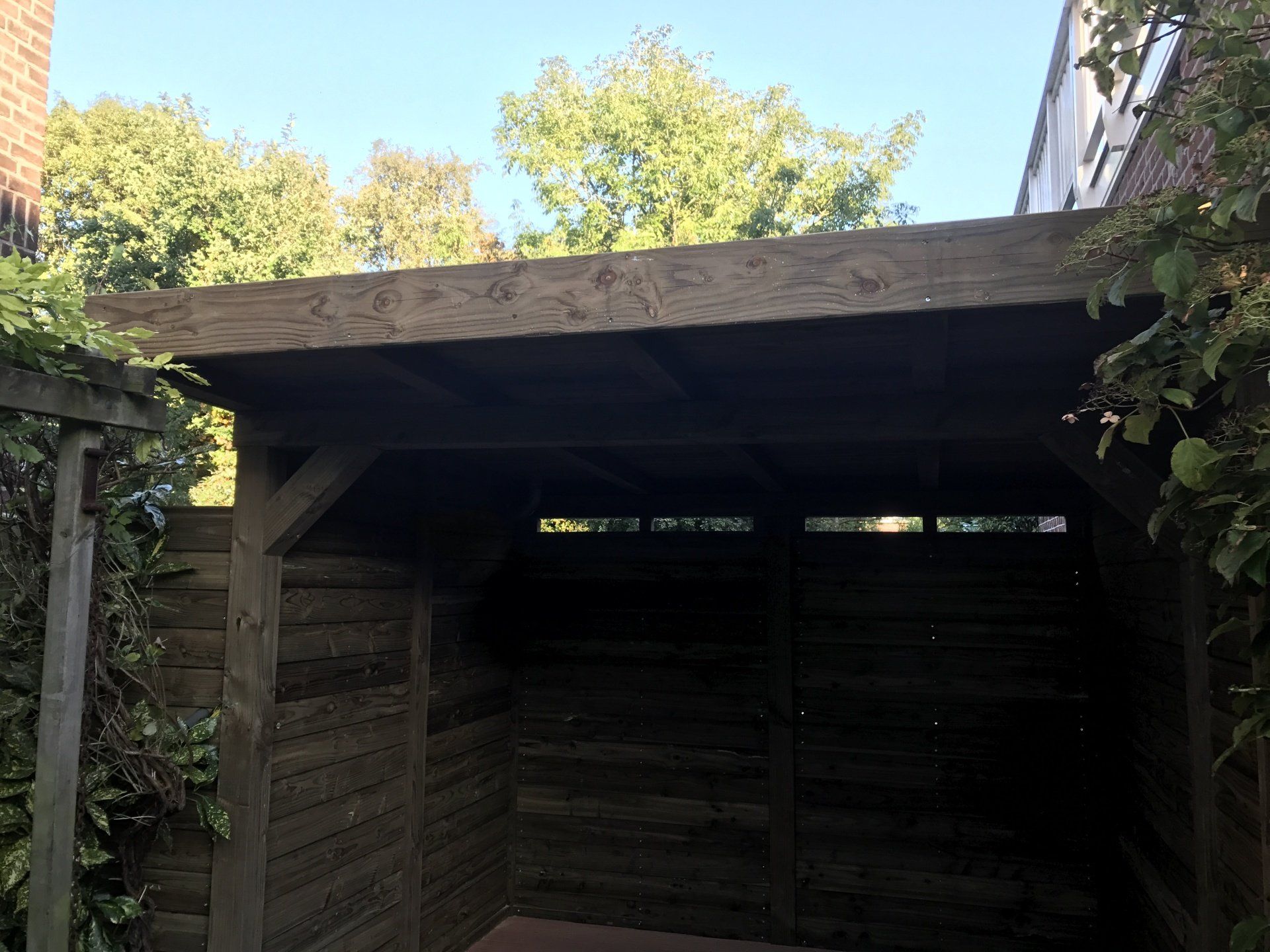 Houten schuur met een plat dak, gelegen op een erf. Zonlicht stroomt naar binnen.