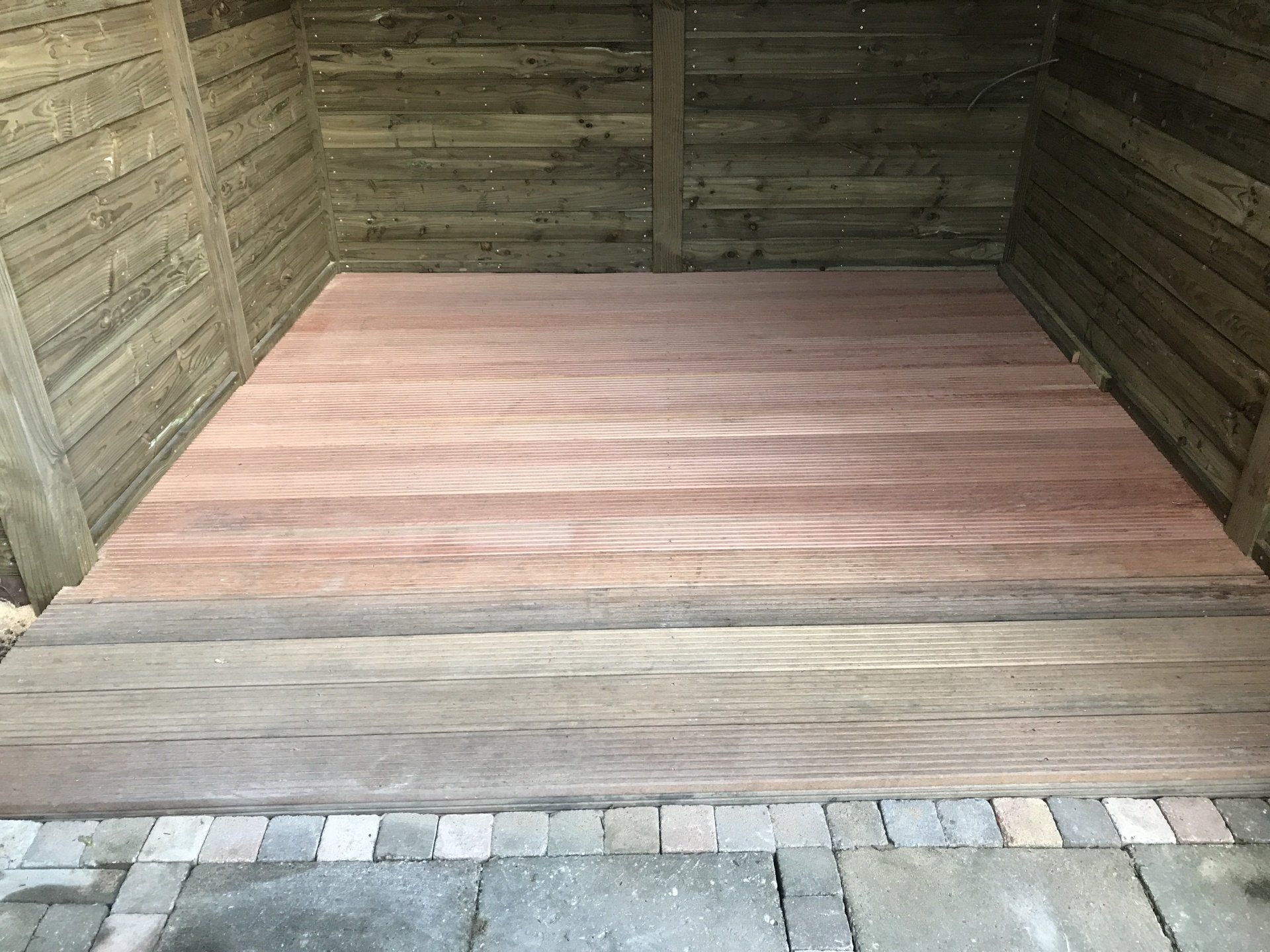 Interieur van een schuur met een roodbruine vloer, houten wanden en een bakstenen rand bij de ingang.