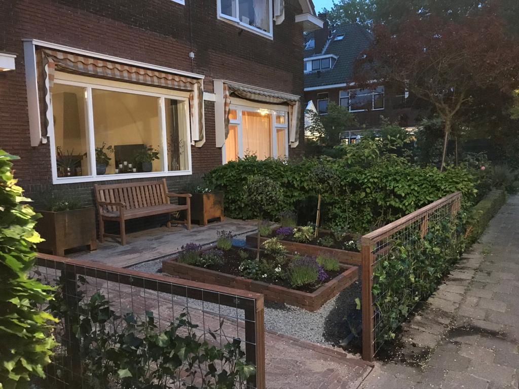 Bakstenen huis met ramen die veel lichtinval geven, een kleine tuin, een bankje en een laag hekje.