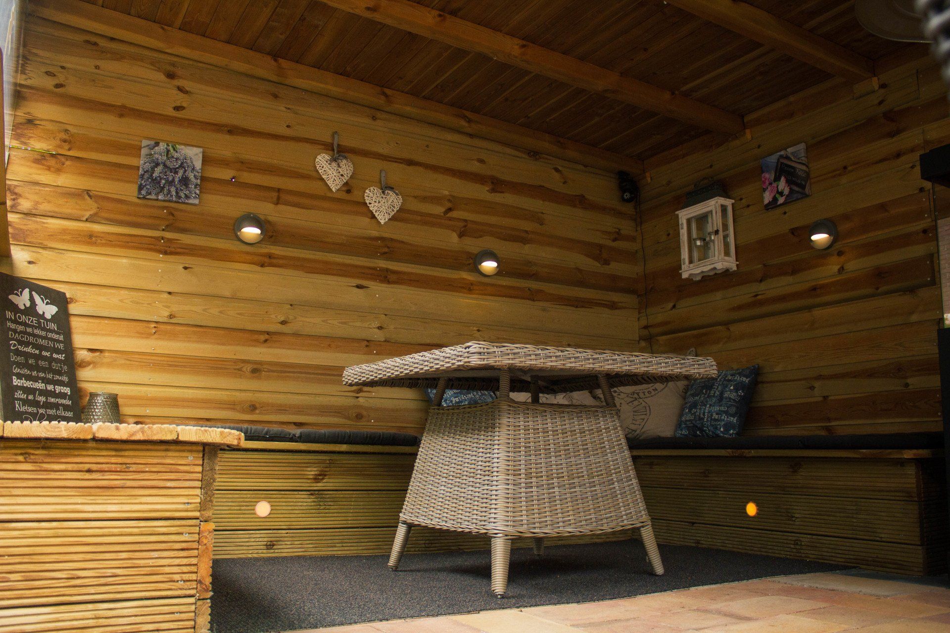 Houten zithoek buiten met rieten tafel, ingebouwde bank en decoratieve wanddecoratie.