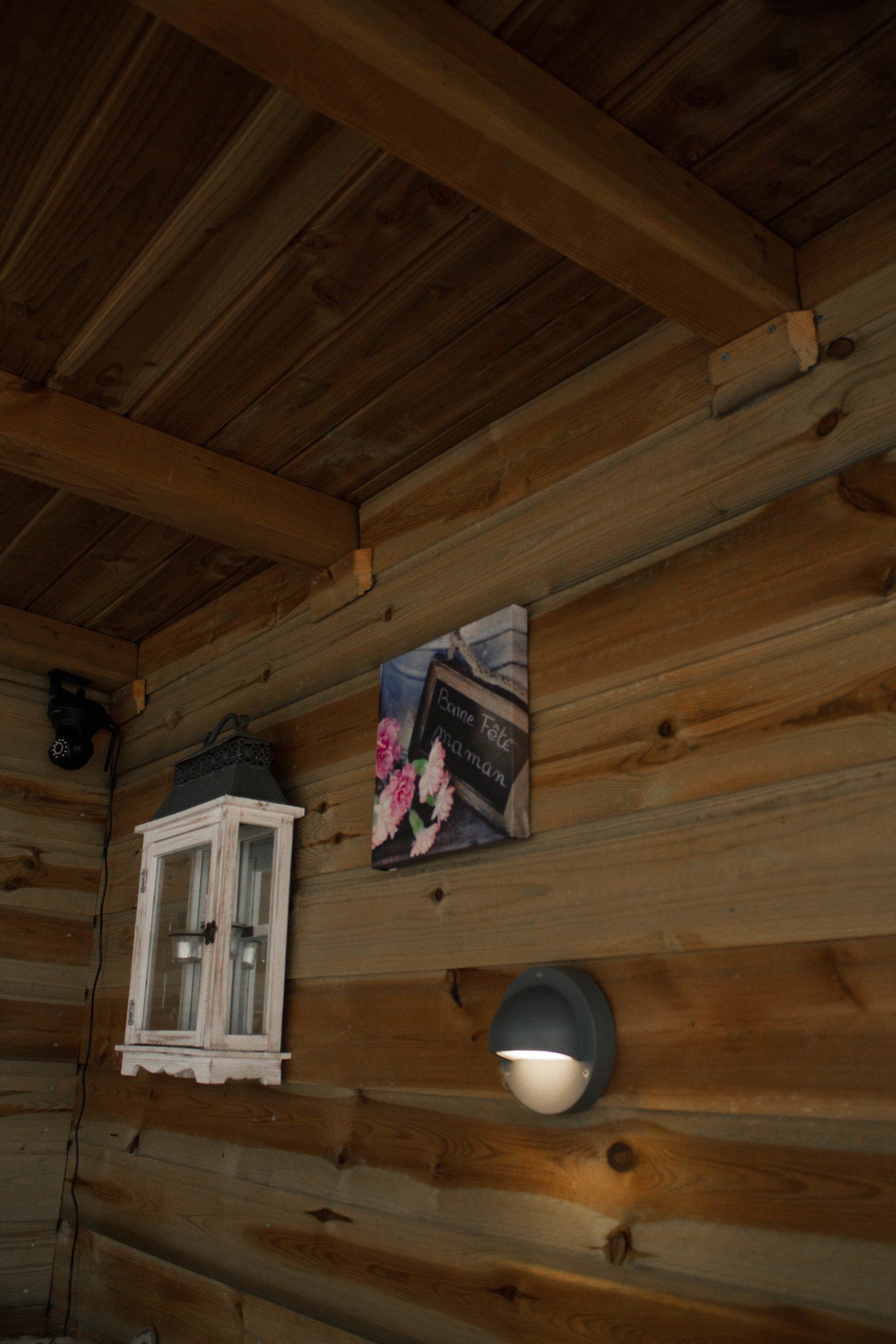 Houten interieur van een blokhut met een witte kast, kunstwerken en een wandlamp.