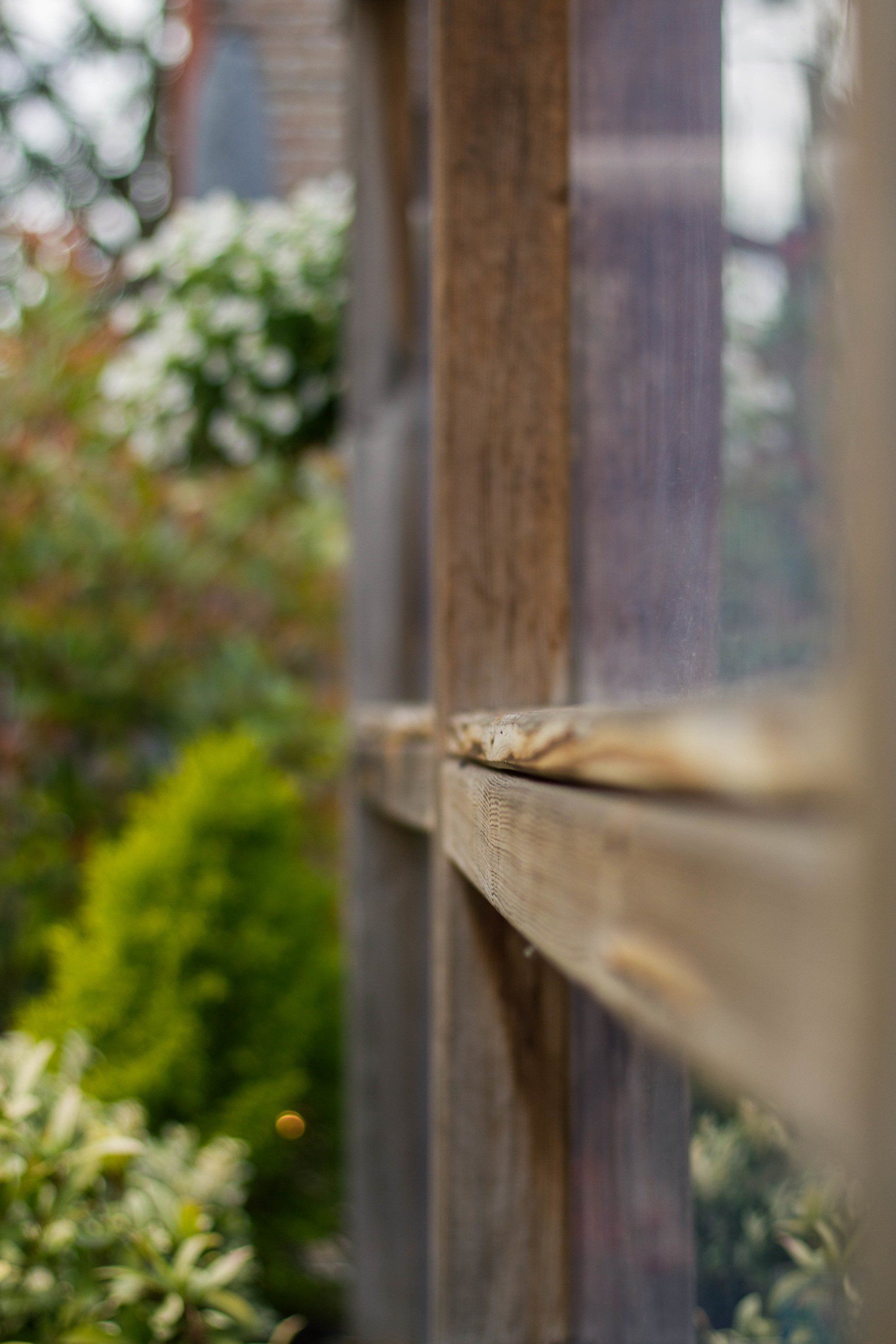 Houten raamkozijn met wazige tuinbegroeiing op de achtergrond.