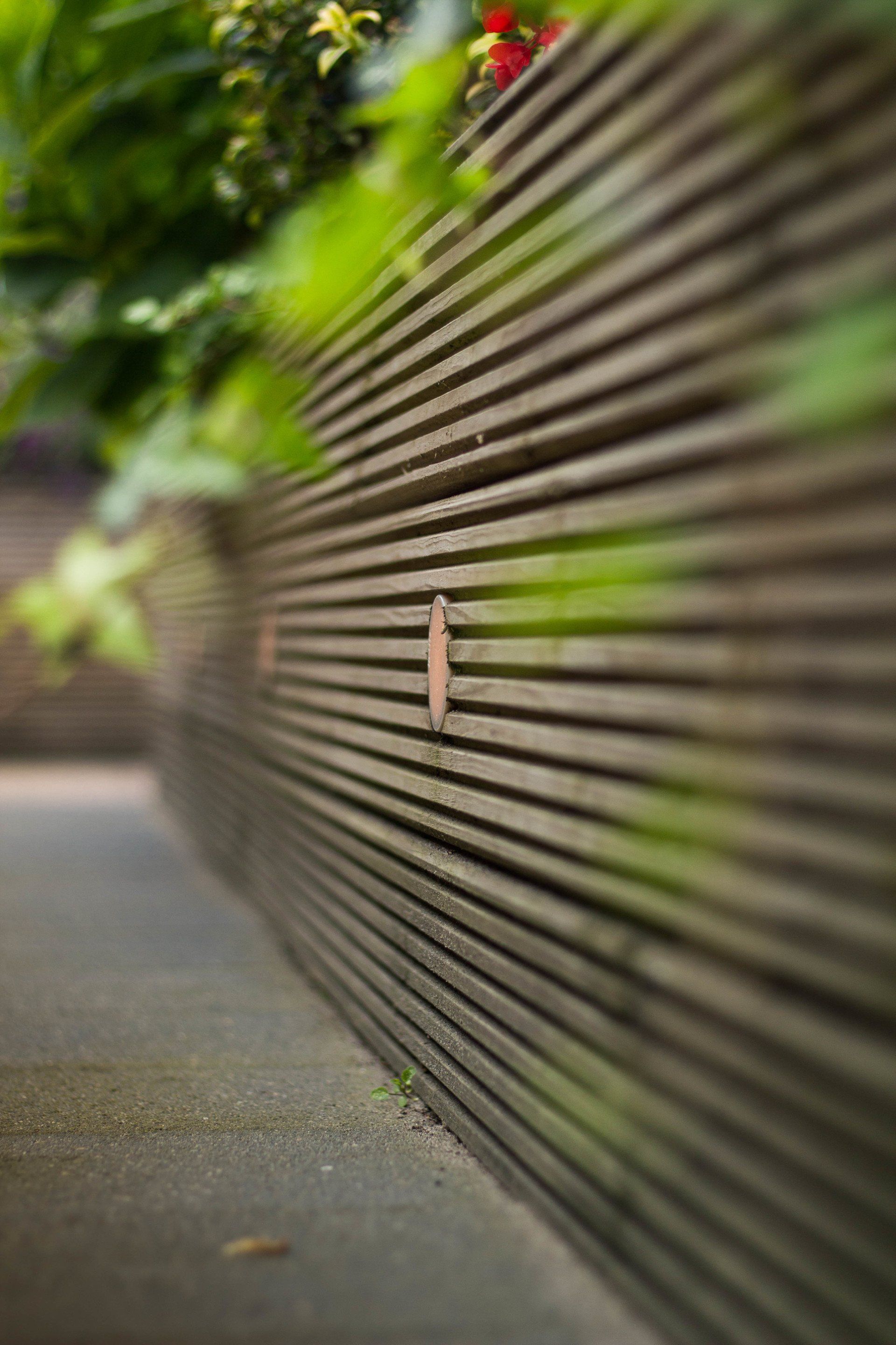 Een houten lattenhek met een klein, plat voorwerp eraan bevestigd; groen op de wazige achtergrond.