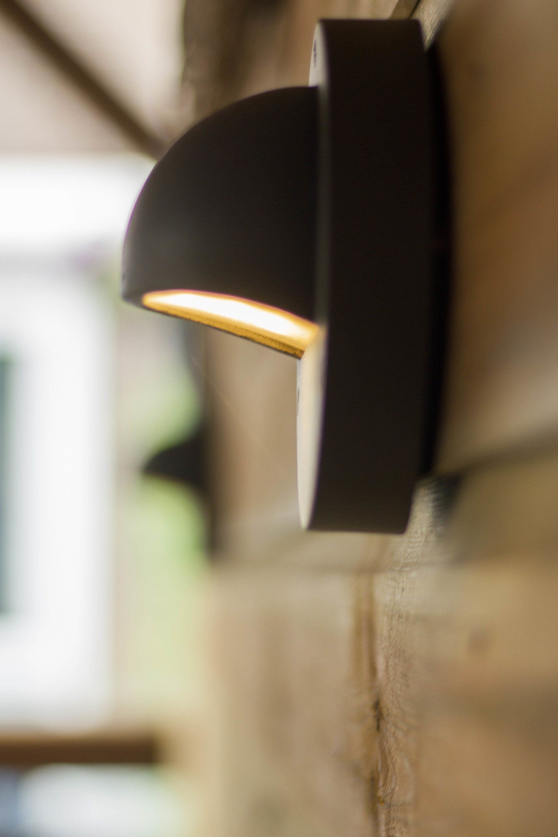 Zwarte, halfronde buitenwandlamp die warm licht uitstraalt op een houten oppervlak.